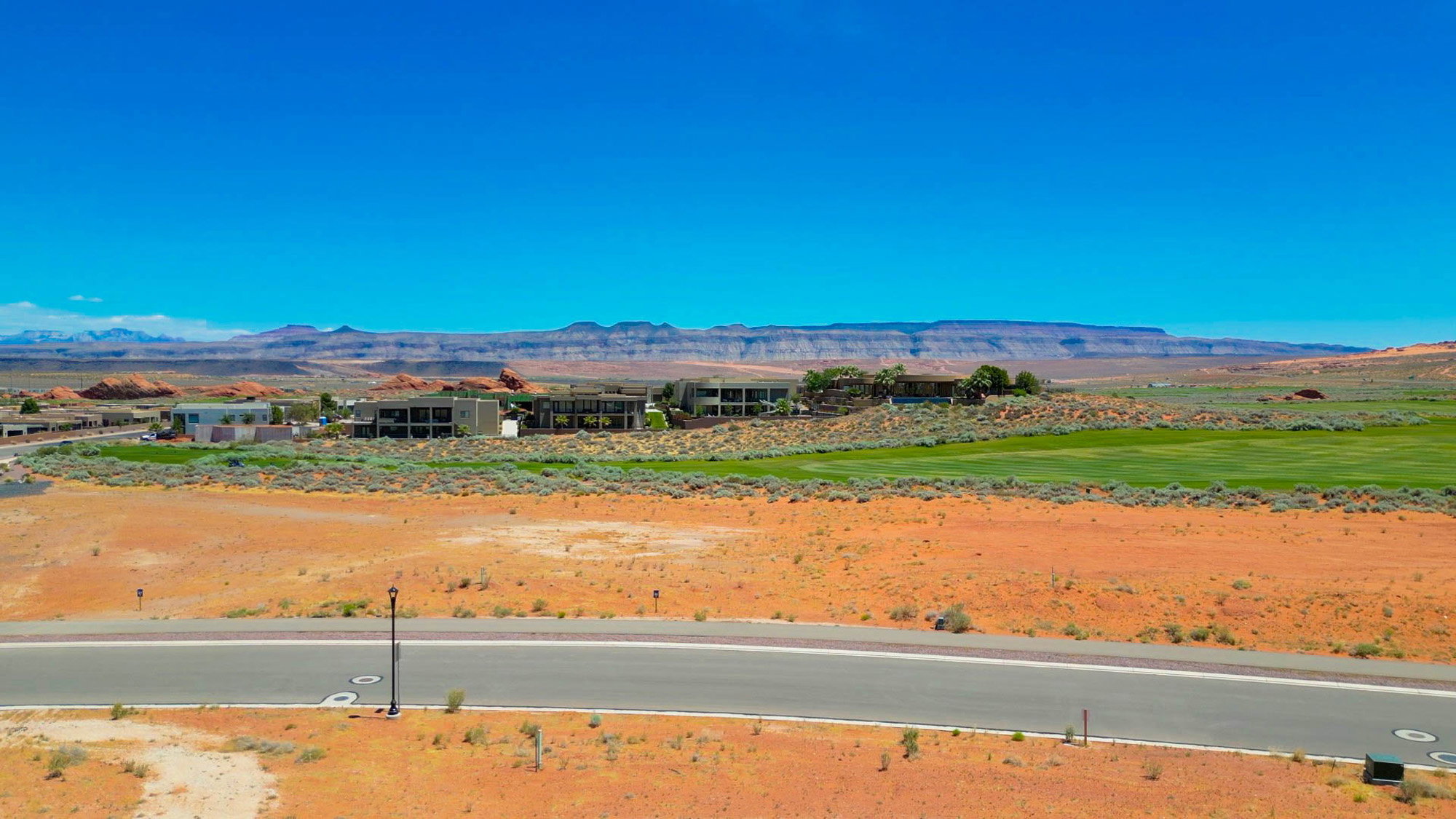 Desert landscape featuring a paved roadway, arid vegetation, and distant mountain ranges