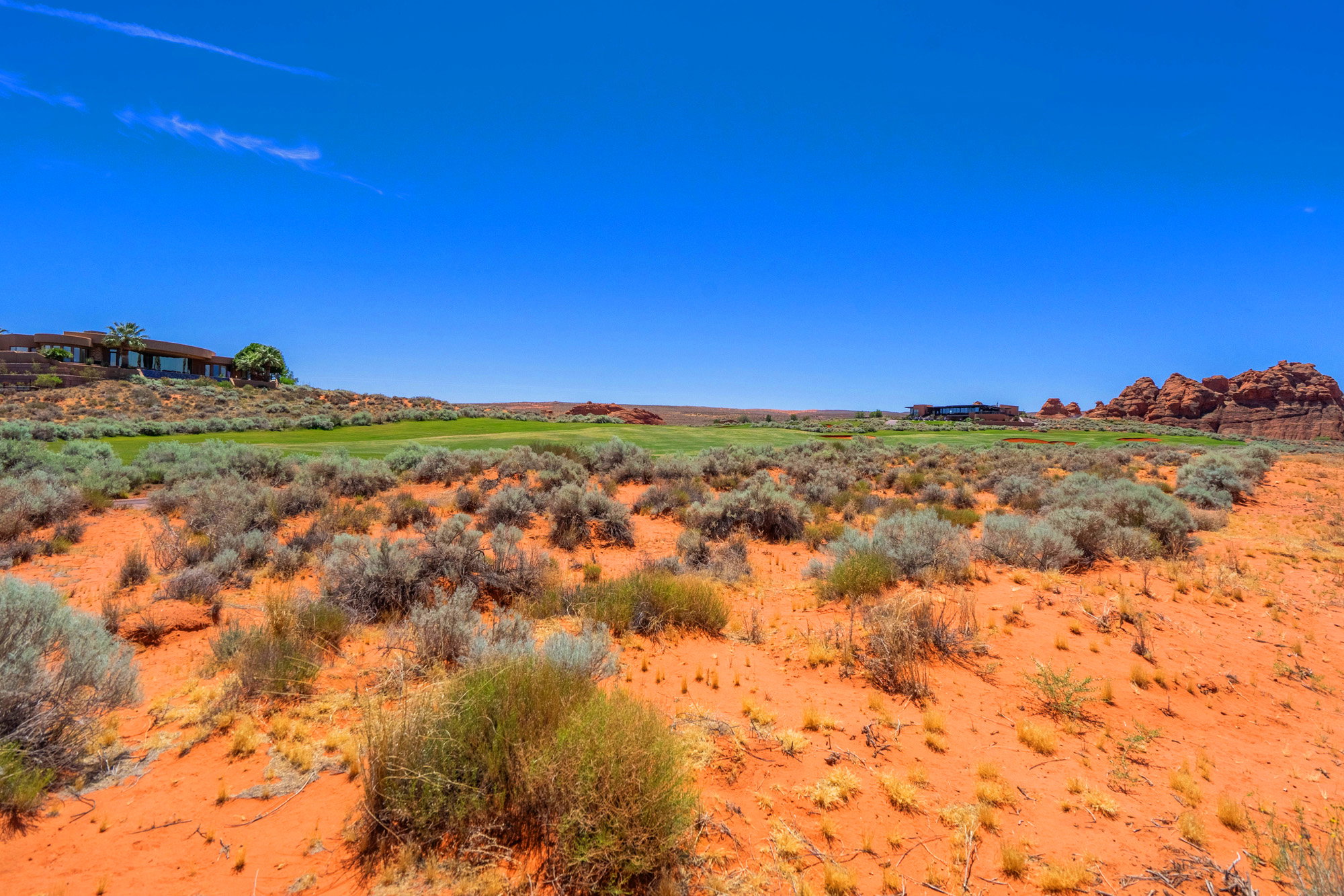 Expansive desert landscape featuring red sand, native shrubs, and a meticulously maintained golf course