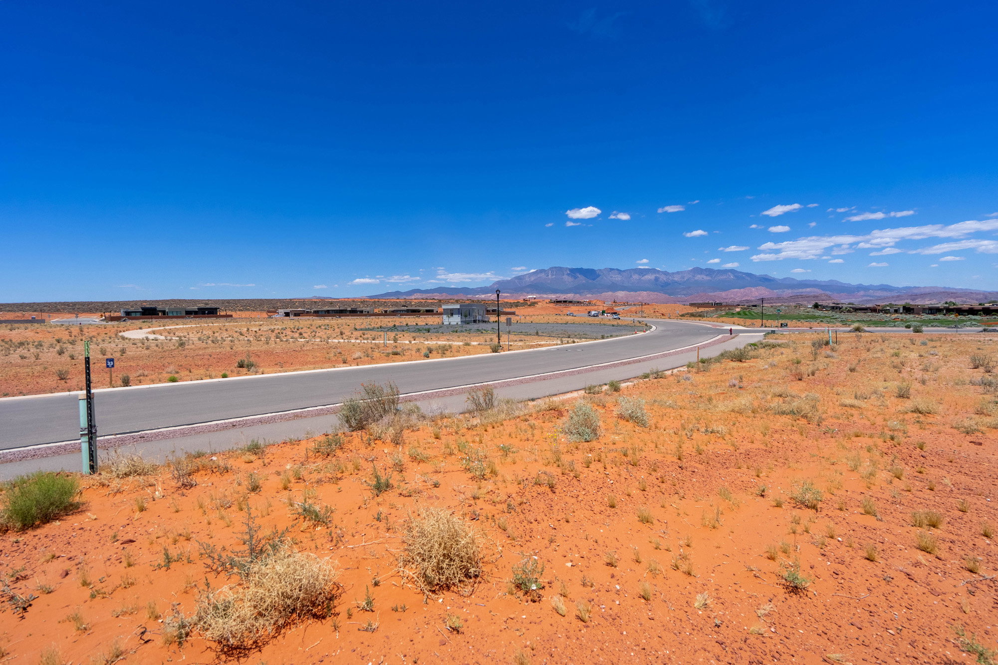 Paved road winding through a desert landscape with distant mountains under a clear blue sky