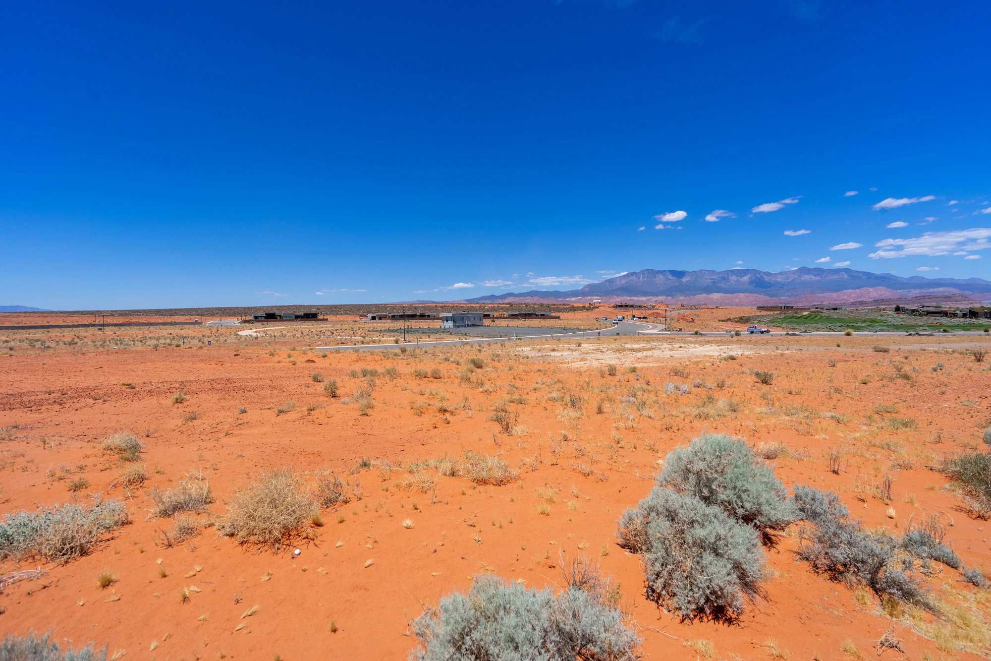 Expansive desert landscape featuring red earth, scattered scrub brush, and distant mountain ranges under a clear blue sky
