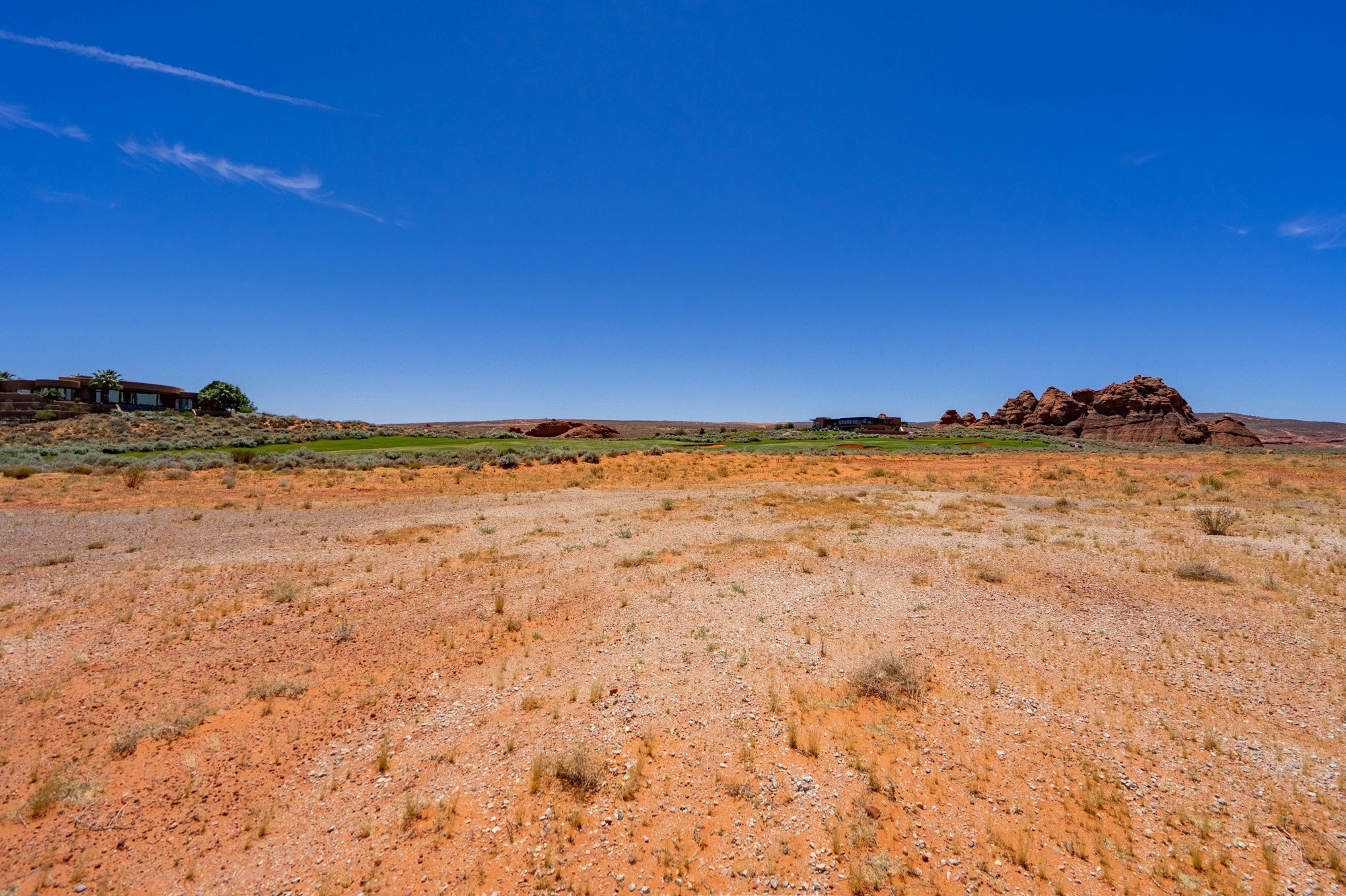 Expansive desert landscape featuring reddish-orange earth and sparse, dry vegetation