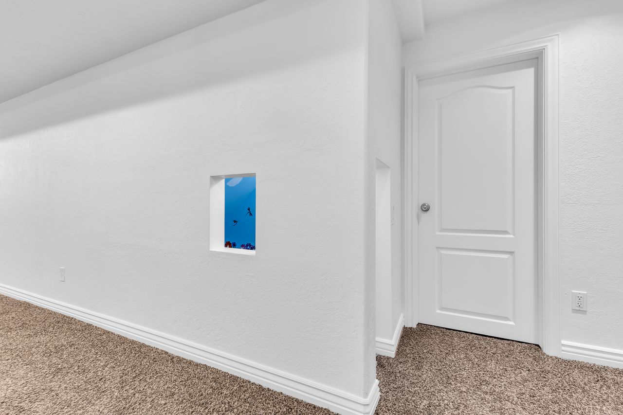 Recessed wall niche with a vibrant blue-sky background, complemented by white walls, textured carpeting, a white two-panel interior door, and clean white baseboards