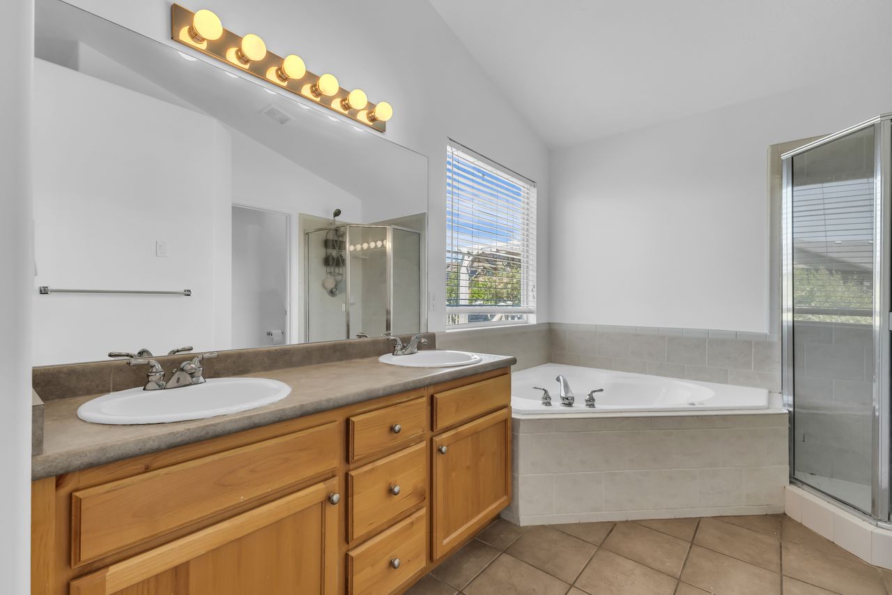 Double vanity with integrated sinks and wood cabinetry, large mirror, and overhead strip lighting