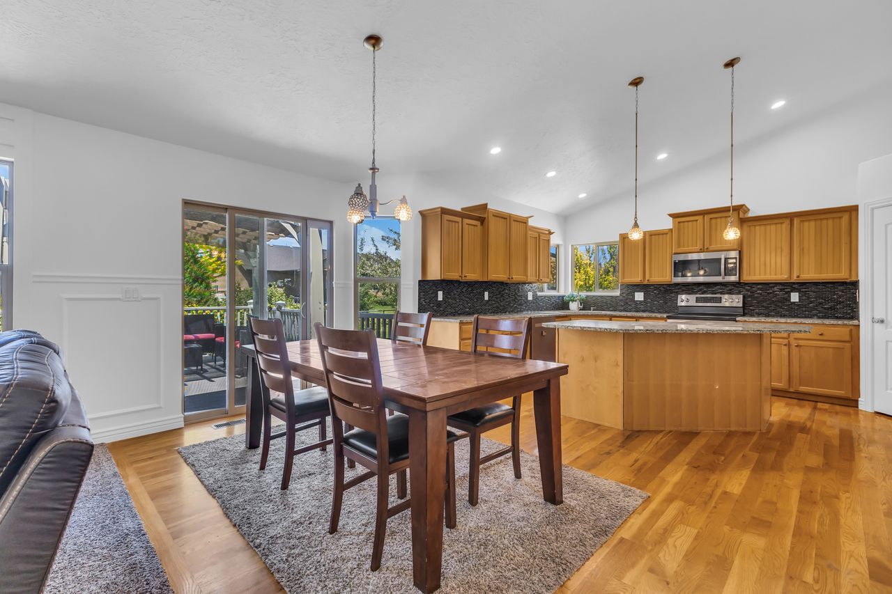 Open-concept living space featuring wood-finish flooring, vaulted ceilings with recessed lighting, and a kitchen with wood cabinetry and a central island