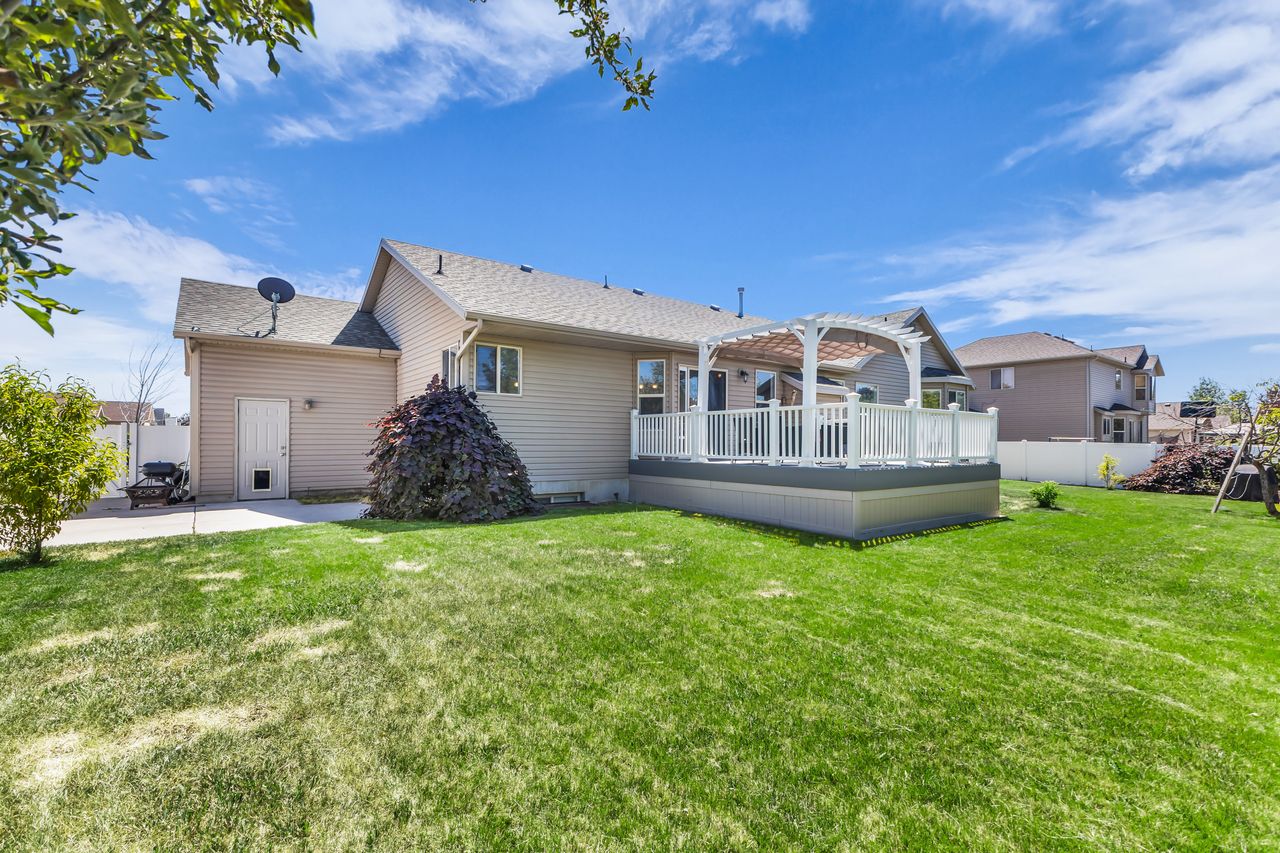 Spacious backyard featuring a large green lawn, an elevated deck with white railings, and an integrated pergola