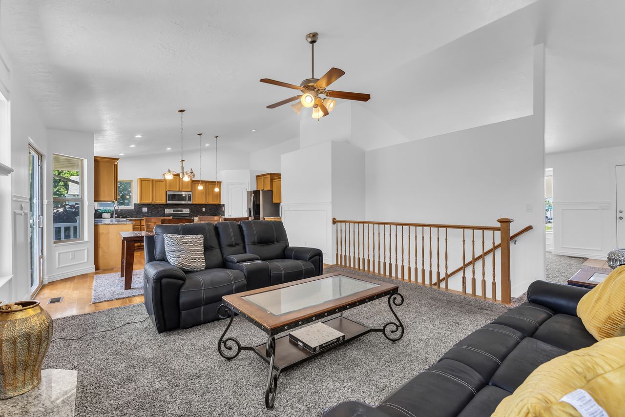 Spacious living area featuring vaulted ceilings, a ceiling fan, and wood railing