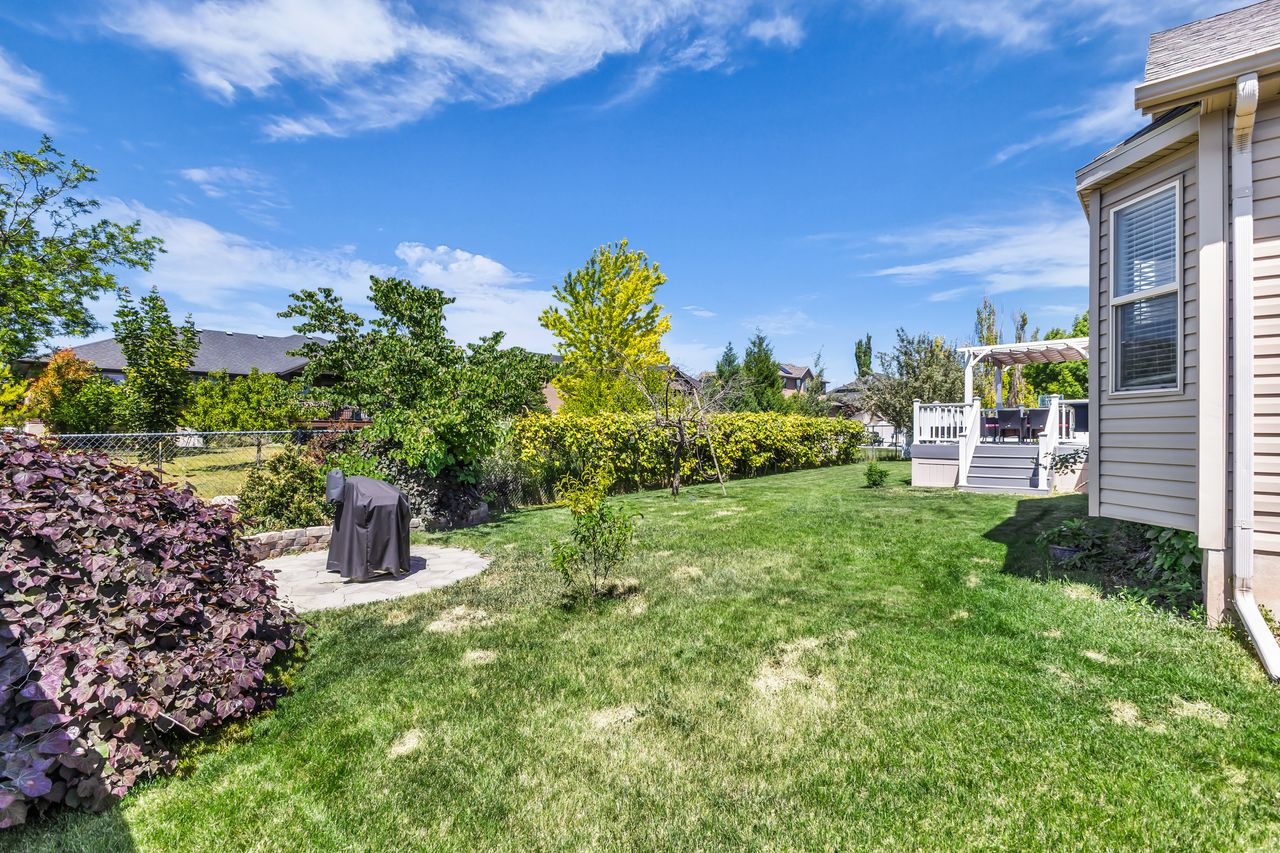 Expansive lawn with established landscaping, a multi-level deck featuring a white pergola, and a circular stone patio