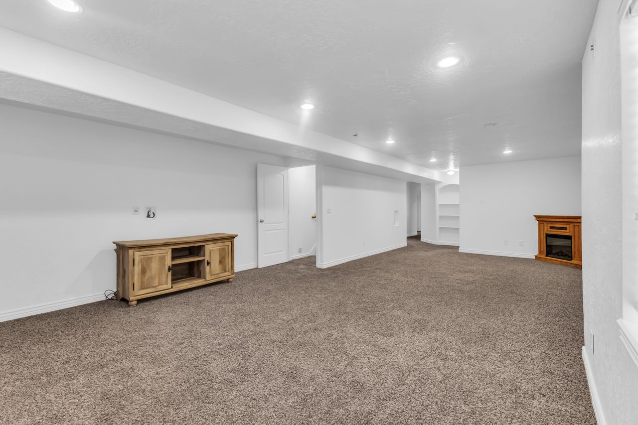 Spacious room featuring plush carpeting, recessed lighting, a built-in electric fireplace, and integrated shelving
