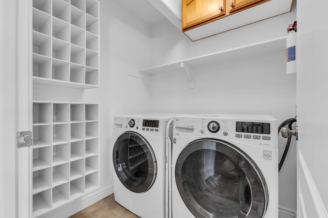 Dedicated laundry area featuring a front-loading washer and dryer, integrated white shelving, and overhead wood cabinetry