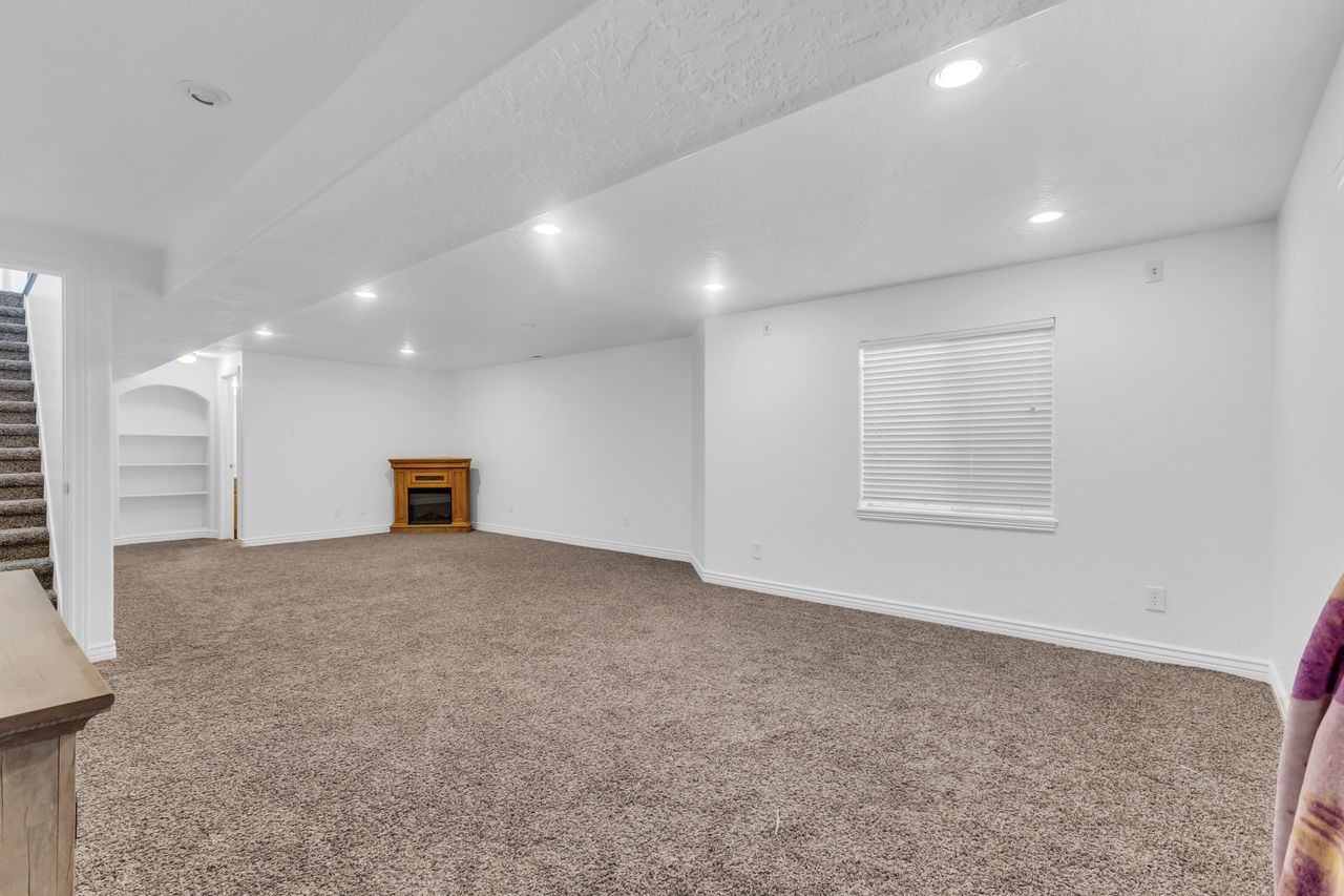 Spacious room featuring neutral carpeting, recessed lighting, built-in shelving, a wood-finish fireplace, and a window with blinds