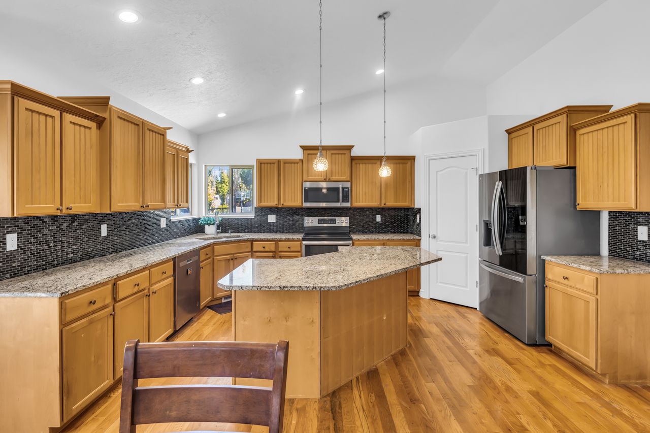 Kitchen featuring wood-finish flooring, light wood cabinetry, stone countertops, and a dark mosaic tile backsplash