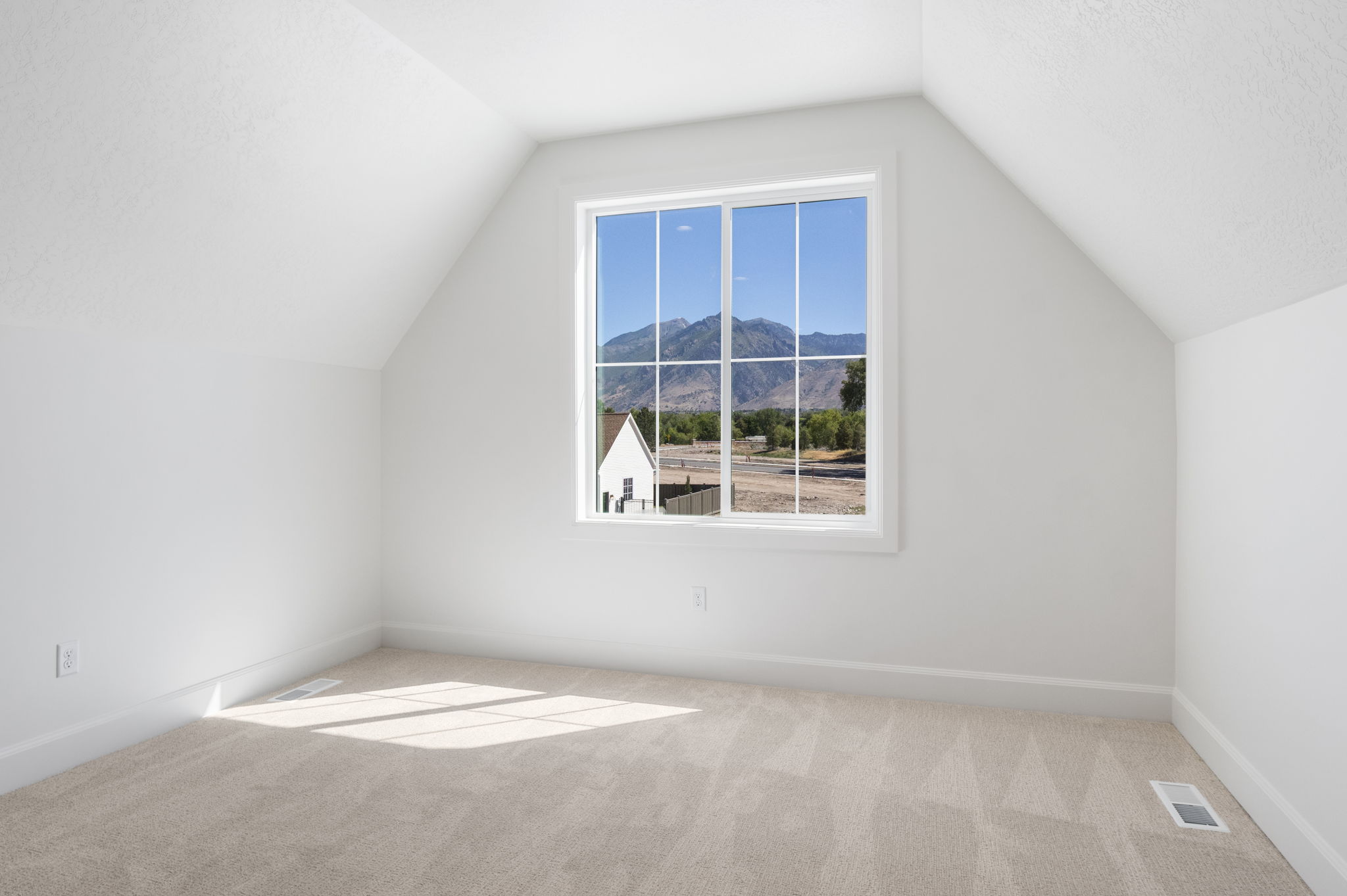 Bright attic space featuring a large multi-pane window, sloped ceilings, plush neutral carpeting, and white baseboards