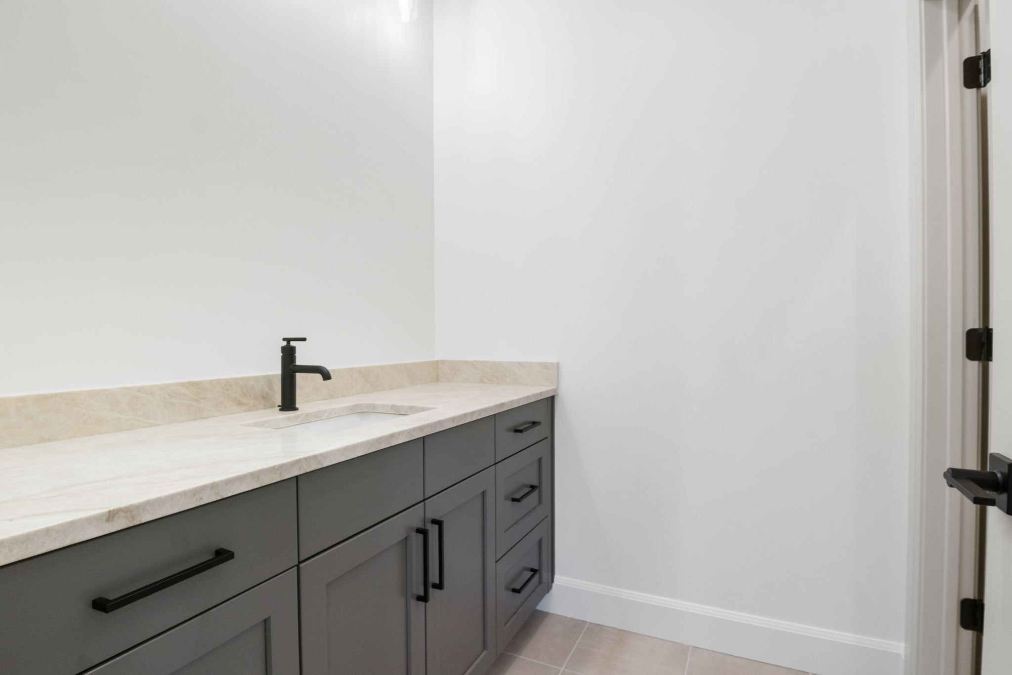 Modern vanity featuring gray cabinetry with matte black hardware, a light-toned countertop, and an integrated rectangular sink with a matte black faucet