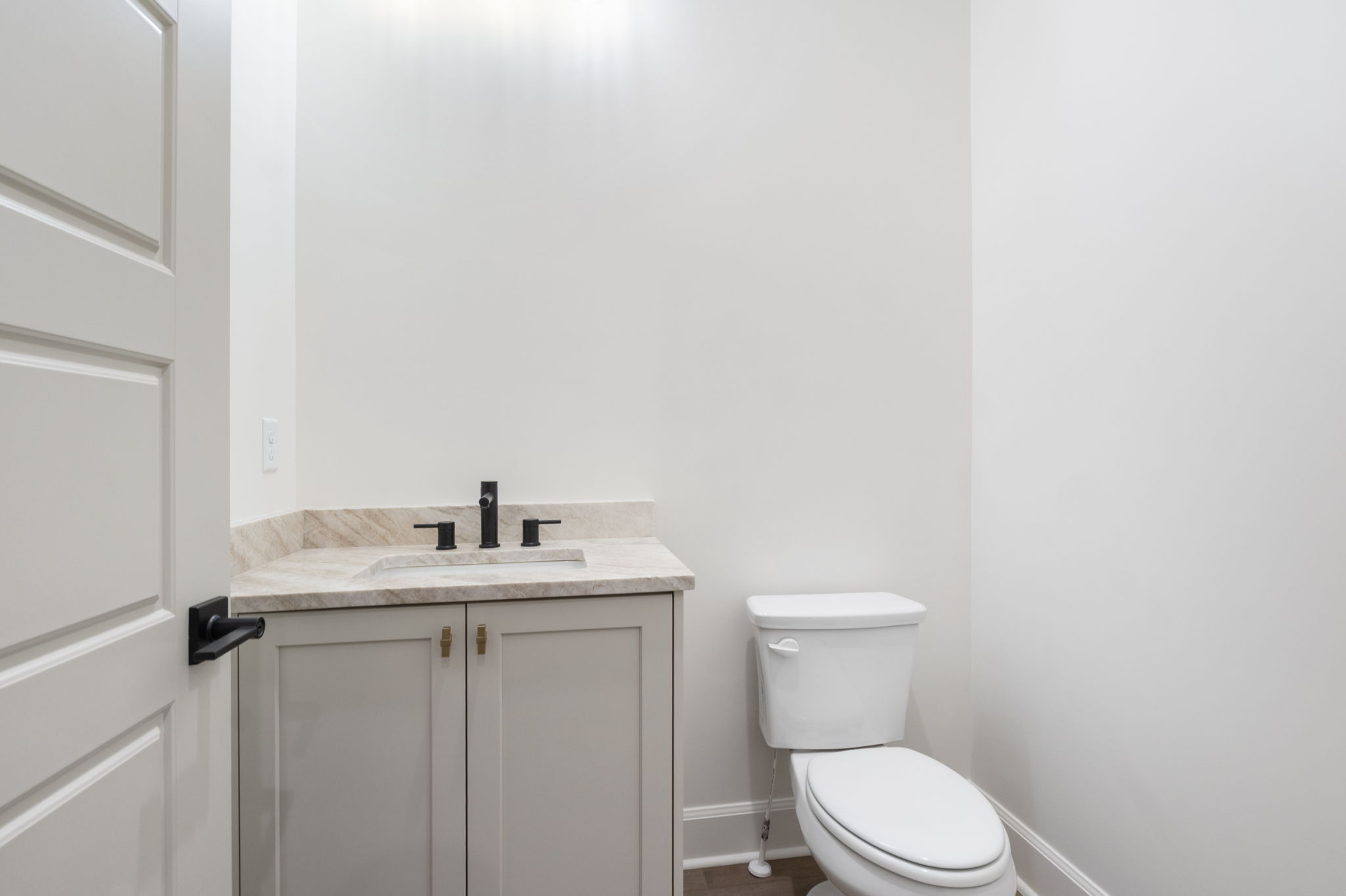 Powder room featuring a light-colored vanity with double doors, stone countertop, integrated sink, and matte black faucet
