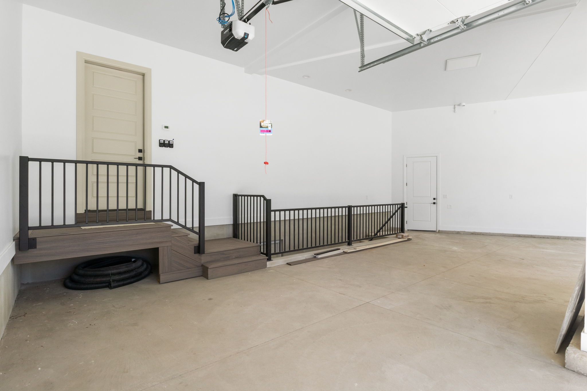 Spacious garage with light grey concrete flooring, white painted walls, and a multi-panel door with dark hardware