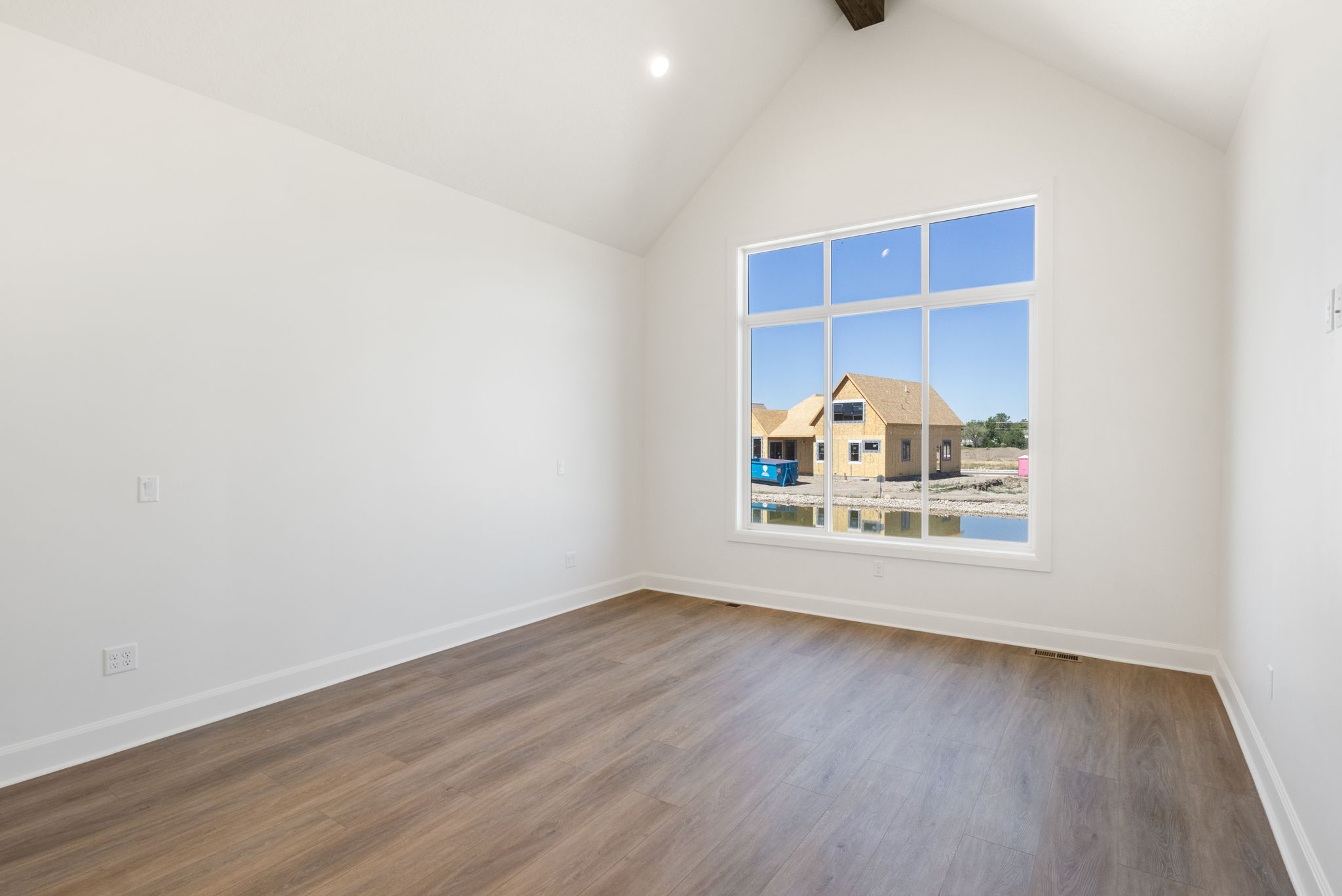 Spacious room featuring a vaulted ceiling with exposed beam, expansive multi-pane window, wood-finish flooring, and white baseboards
