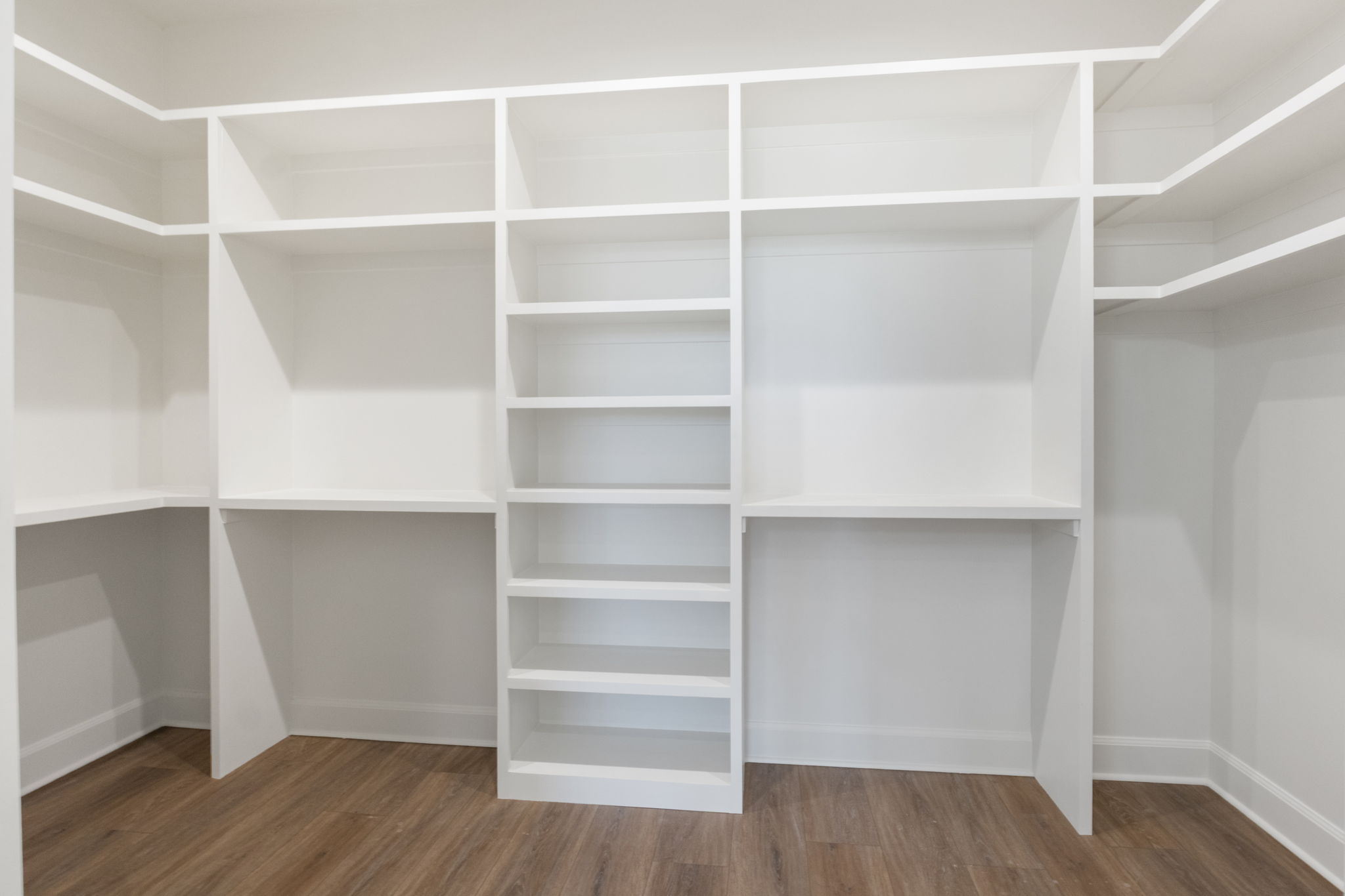 Built-in white shelving system with varied compartment sizes, wood-finish flooring, and white baseboards