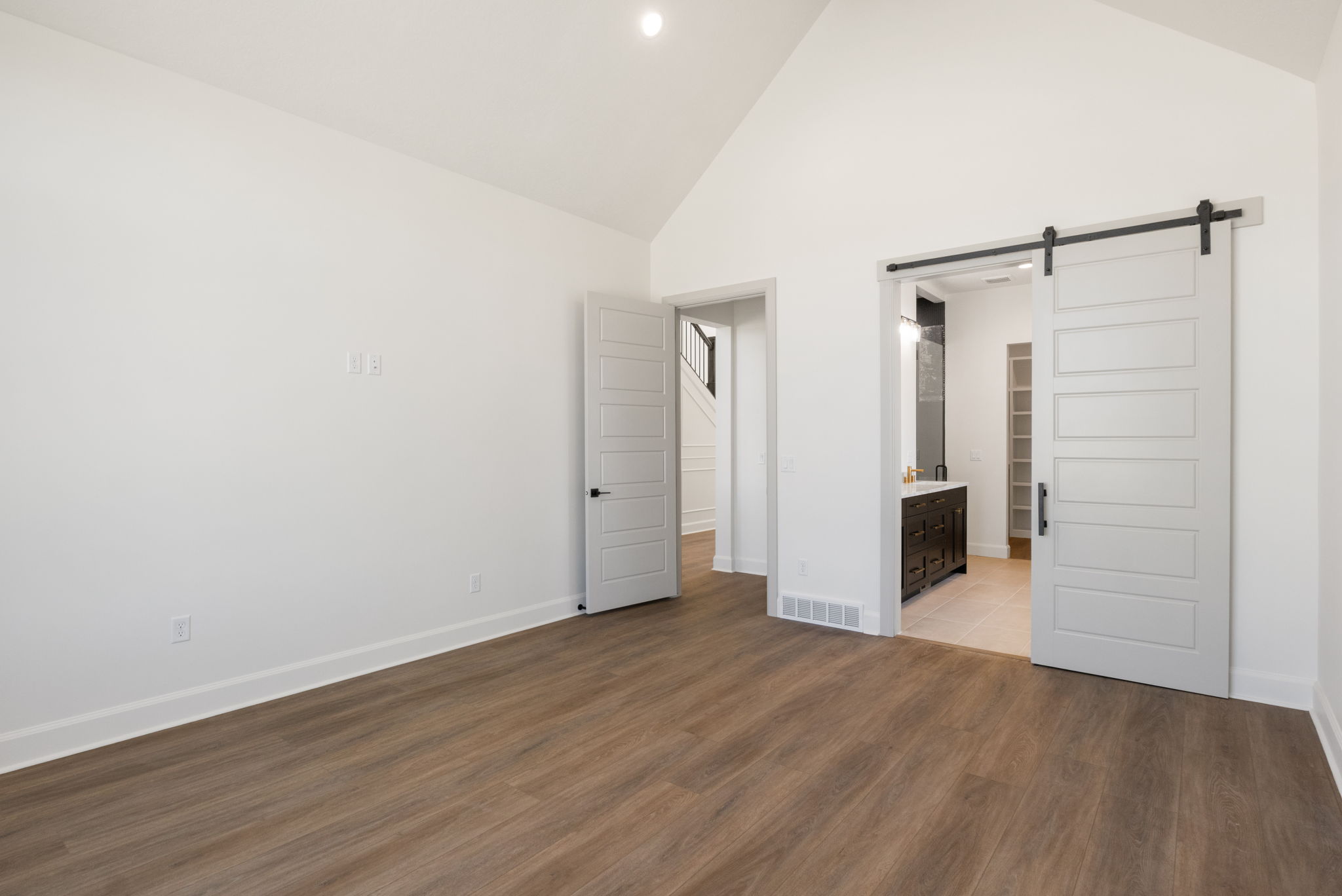 Spacious room featuring vaulted ceilings, wood-finish flooring, and crisp white walls