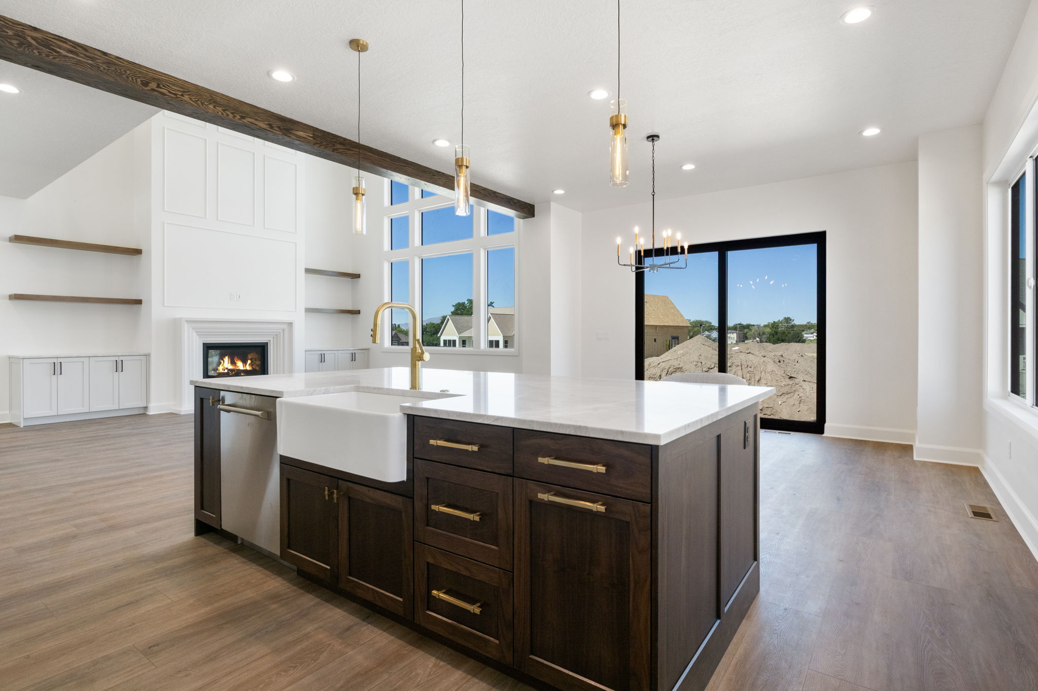 Spacious kitchen island featuring a white farmhouse sink, stainless steel dishwasher, and dark wood-finish cabinetry with brass hardware