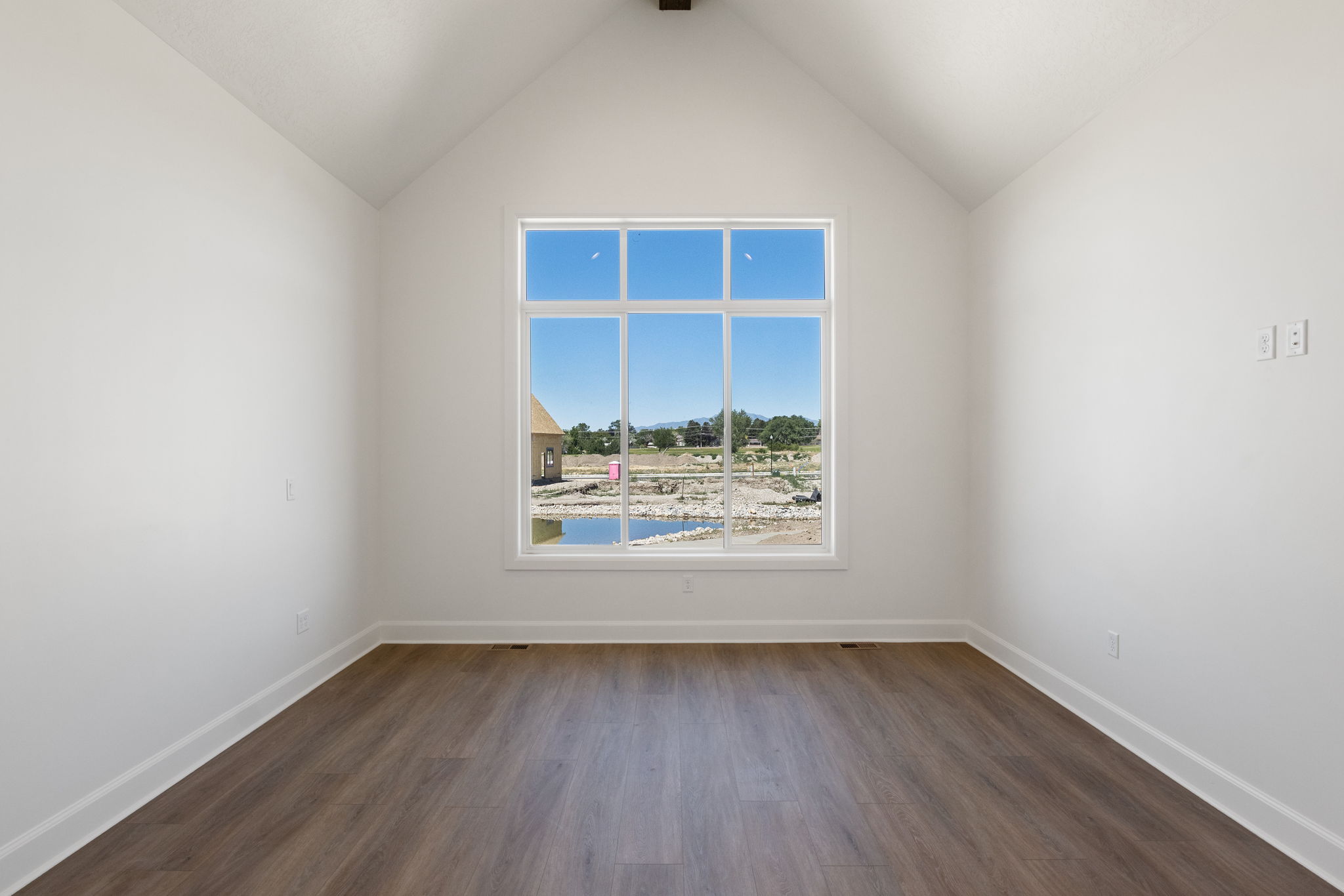 Vaulted ceiling room with wood-finish flooring, white baseboards, and a large multi-pane window