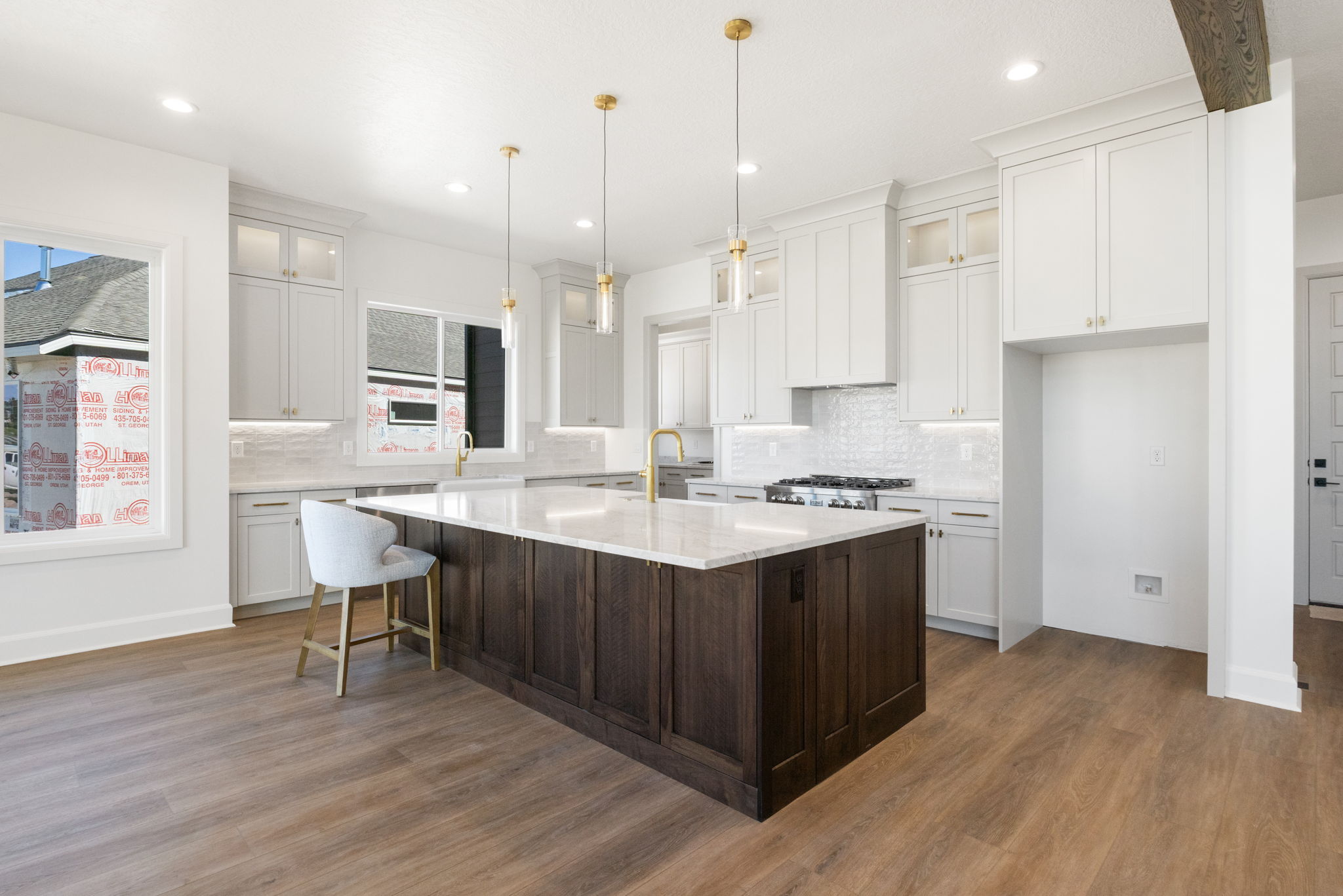 Open-concept kitchen featuring an expansive island with a stone countertop, white shaker cabinetry, gold-finish hardware and fixtures, and wood-finish flooring