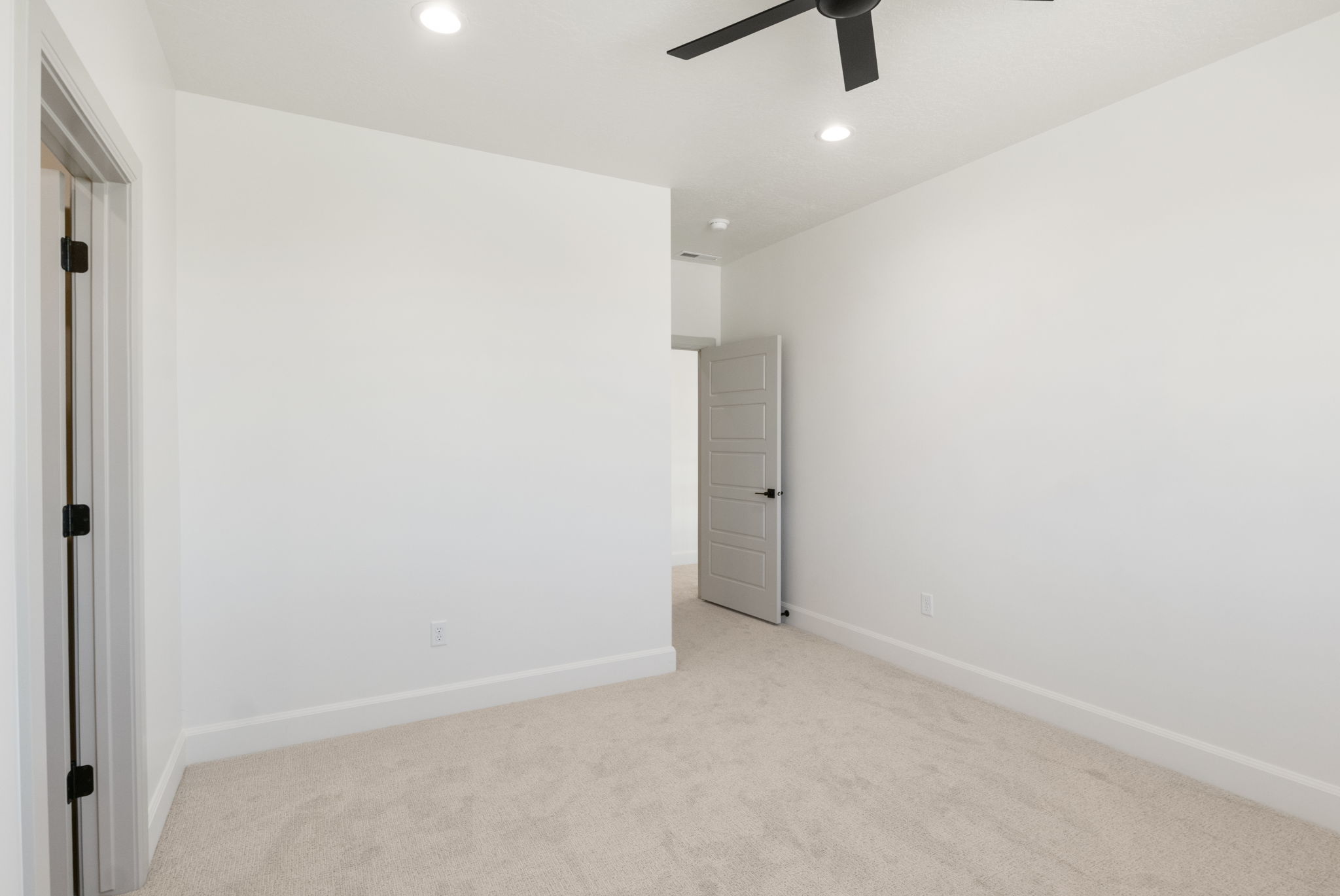 Carpeted room featuring a ceiling fan with integrated lighting, recessed ceiling lights, a paneled interior door with matte black hardware, and crisp white baseboards