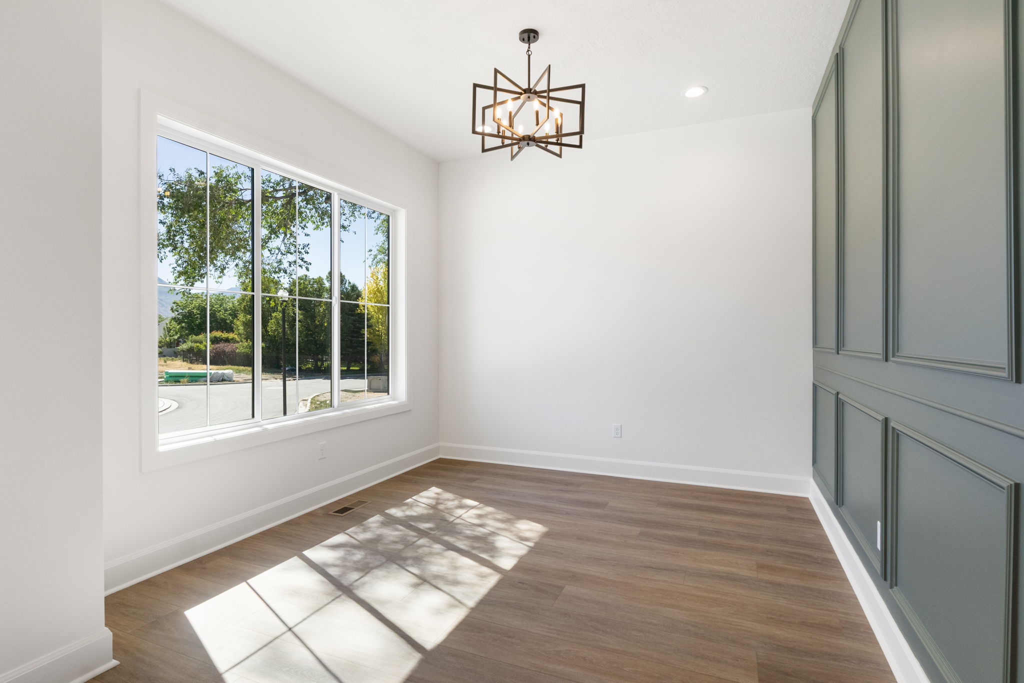 Expansive picture window with white trim, wood-finish flooring, custom accent wall paneling, recessed lighting, and a contemporary chandelier