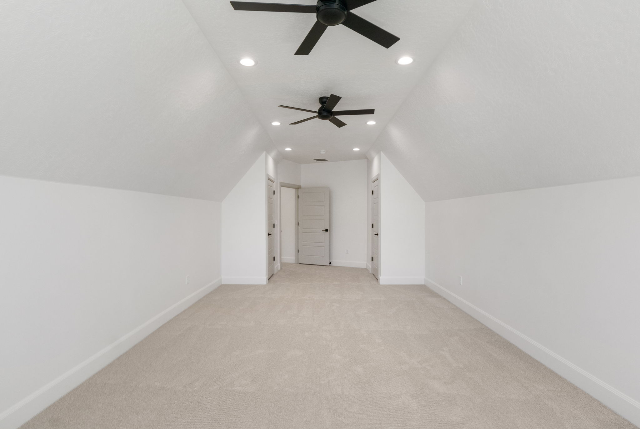 Spacious room with sloped ceilings, two ceiling fans, recessed lighting, neutral carpet, and white trim