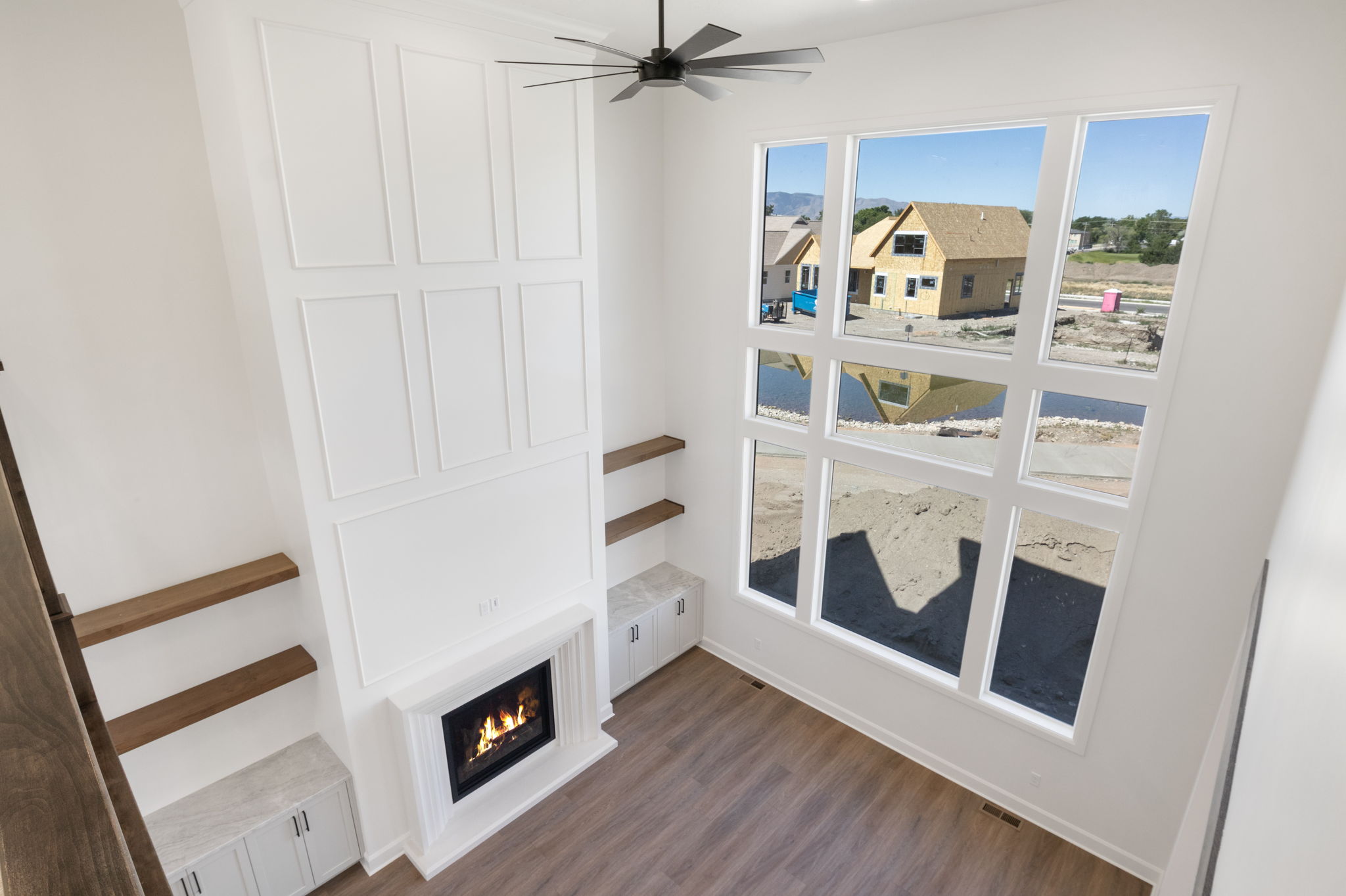 Two-story living area featuring a white paneled fireplace surround with a gas insert, wood-finish flooring, a contemporary ceiling fan, and large multi-pane windows