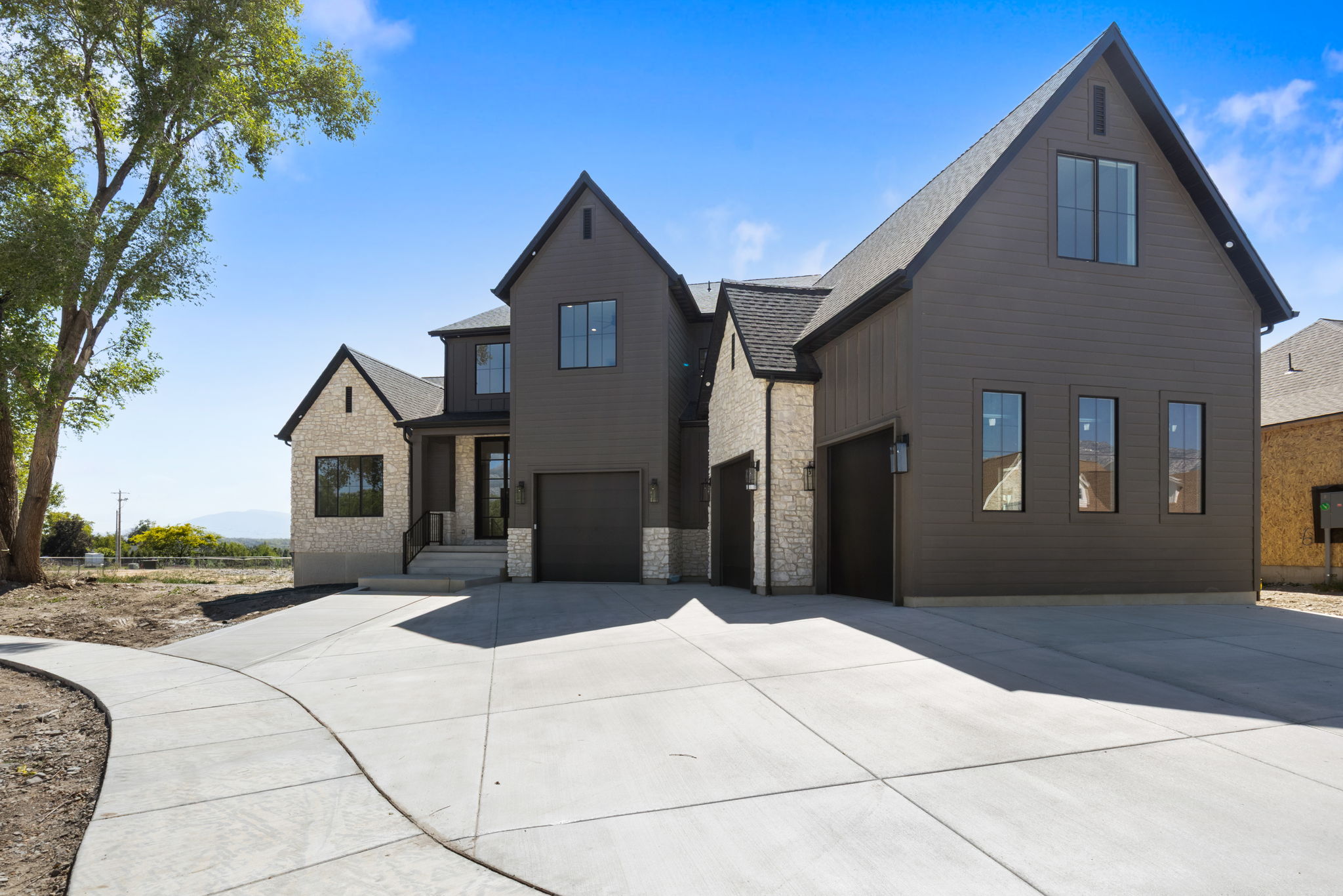 Modern farmhouse-style exterior featuring dark siding, stone accents, black-framed windows, and multiple gables