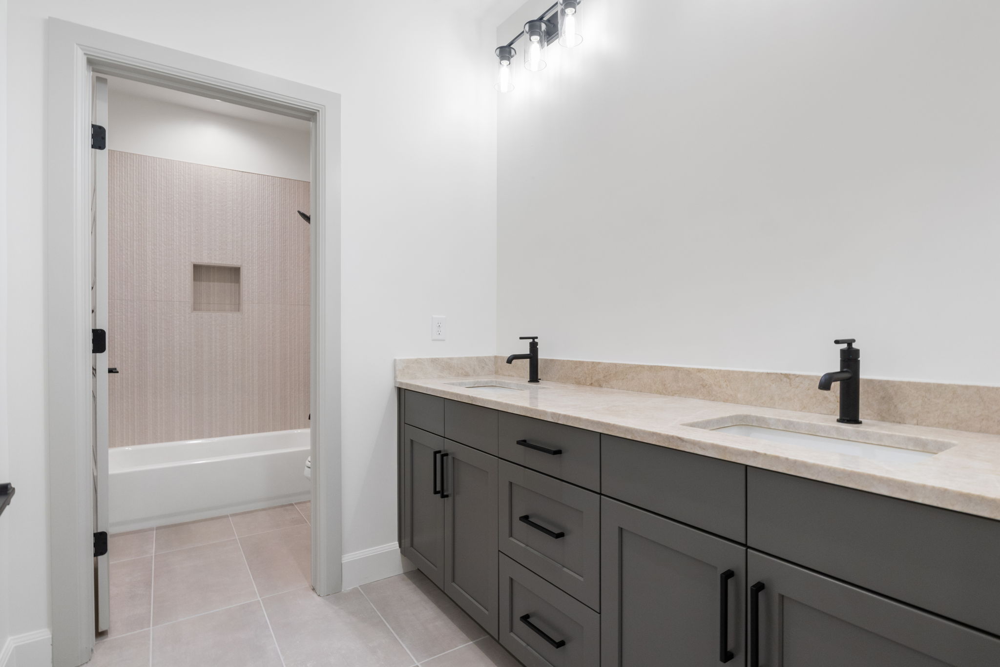 Dual sink vanity featuring dark gray cabinetry, light stone countertop, and matte black fixtures