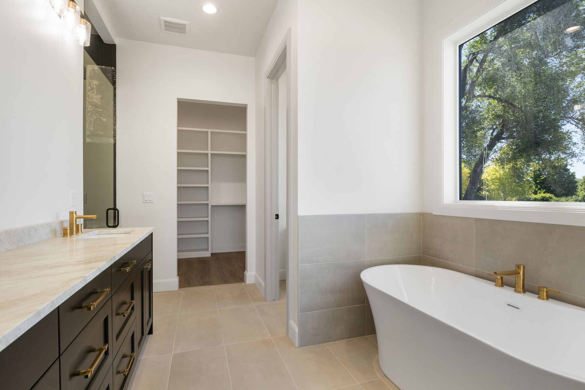 Freestanding soaking tub with gold-finish fixtures and a large window