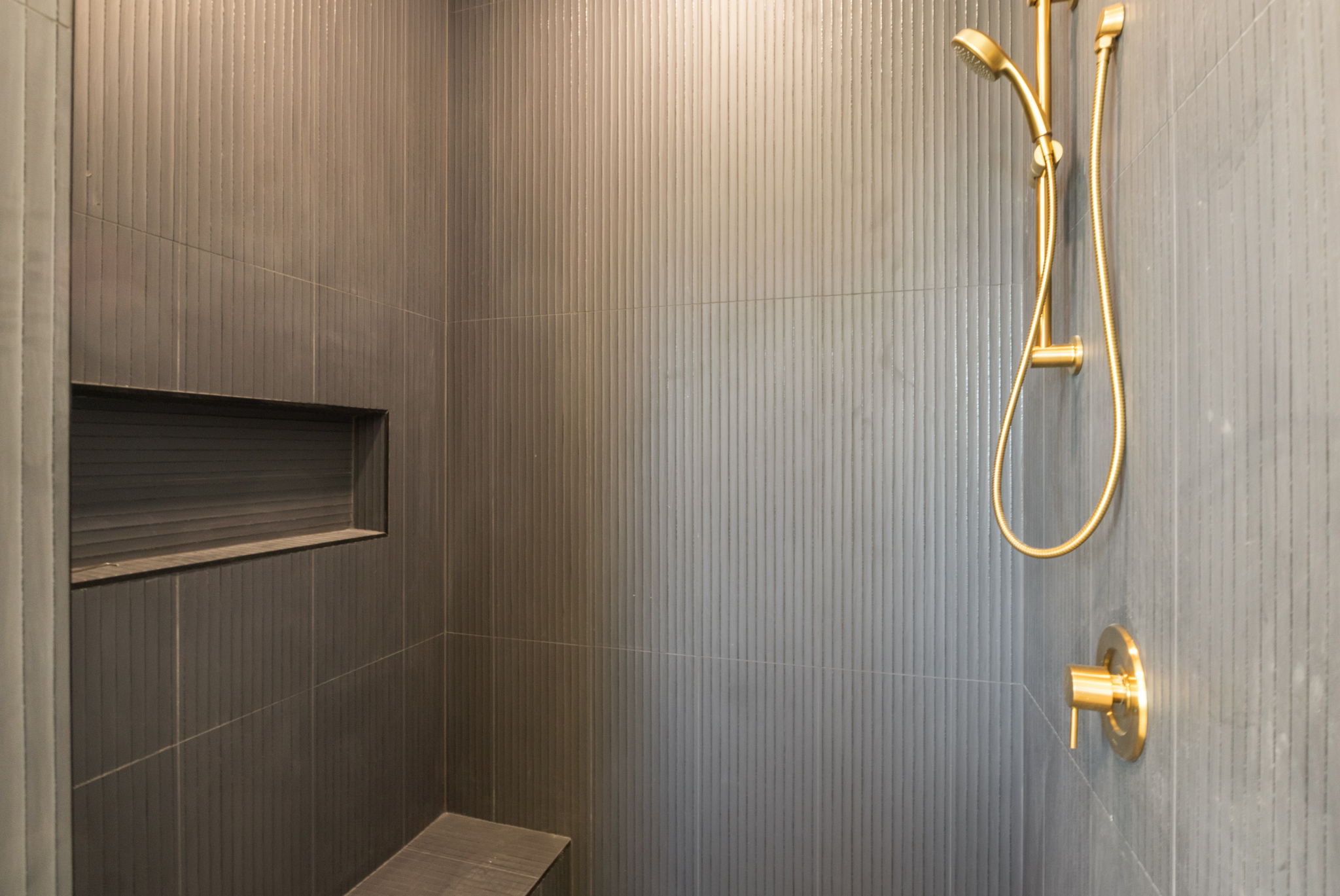 Shower stall featuring matte gold fixtures, a built-in bench, a recessed niche, and vertical-ribbed wall tiling