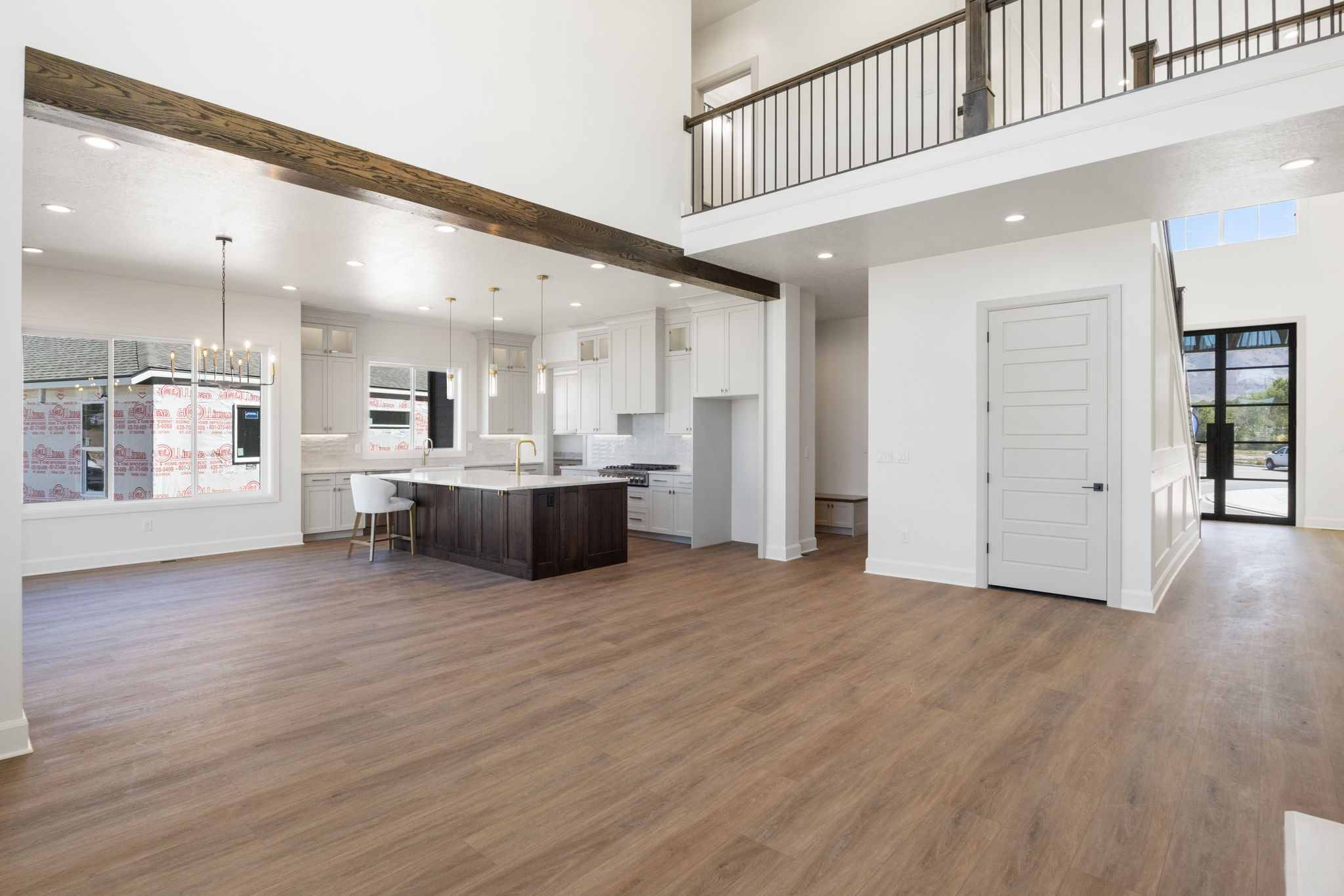 Open-concept living space featuring wood-finish flooring, a two-story ceiling, and a kitchen with white cabinetry, a dark wood island, and pendant lighting