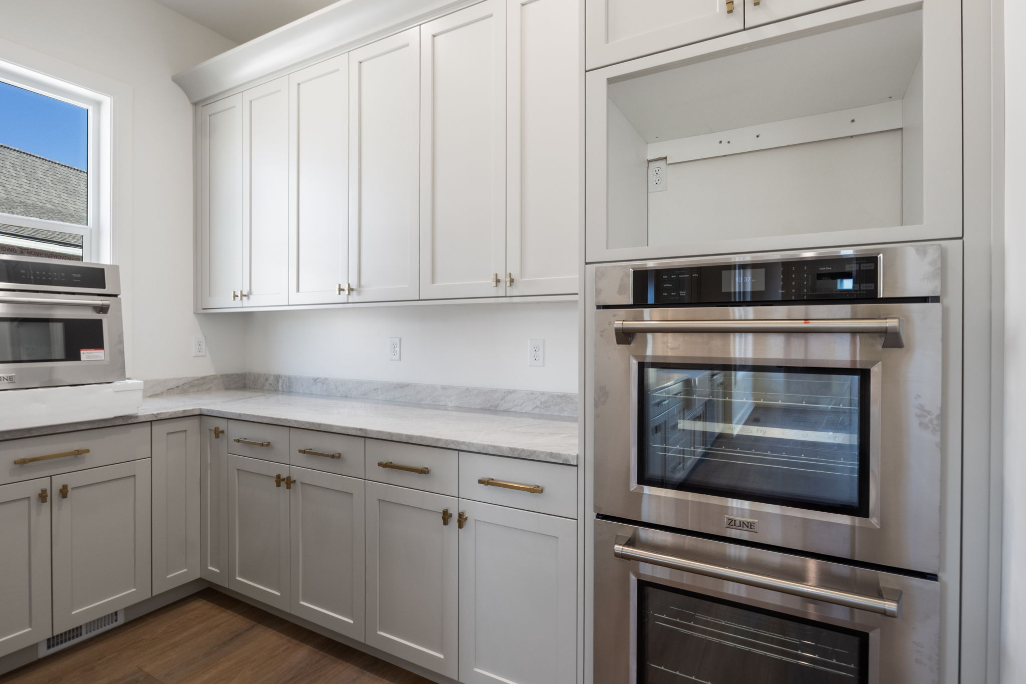 Kitchen featuring white shaker-style cabinetry, light-toned countertops, wood-finish flooring, a built-in stainless steel double oven, and a built-in stainless steel microwave