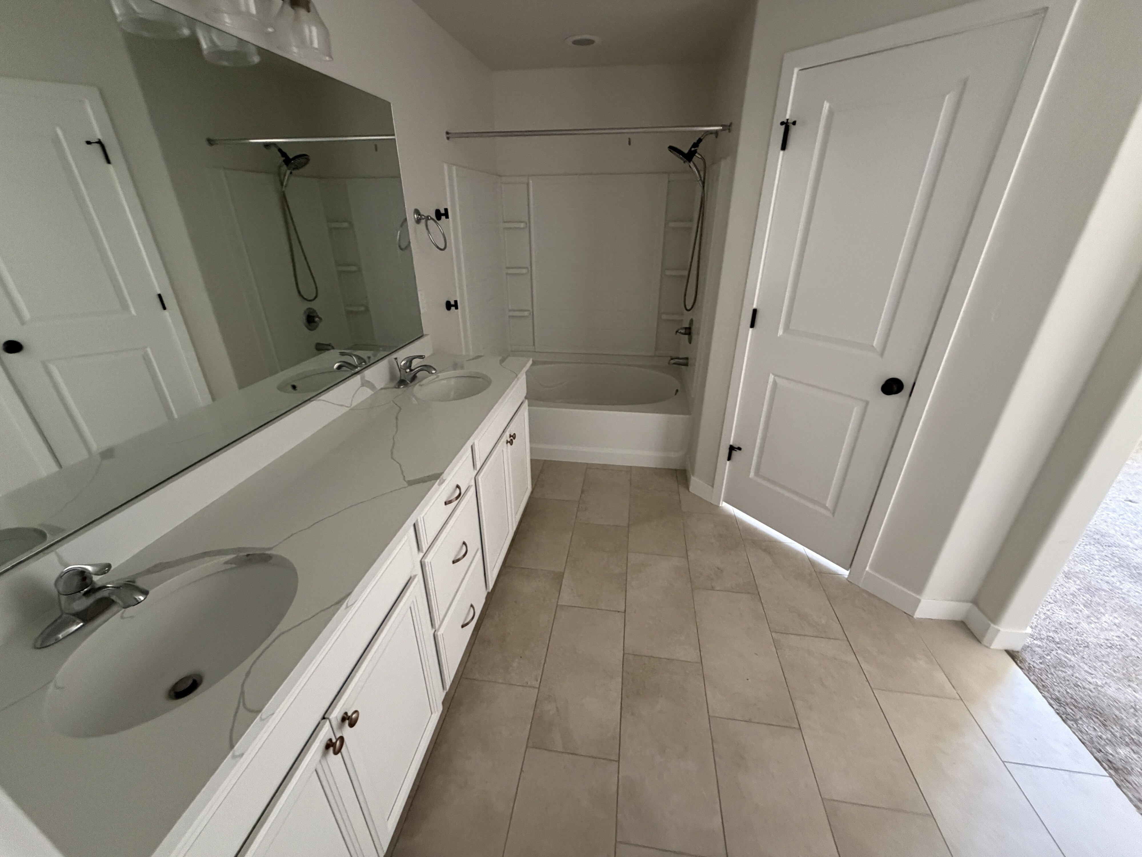 Bathroom featuring a dual-sink vanity with a light-toned countertop, a full-width mirror, and an integrated bathtub with a shower
