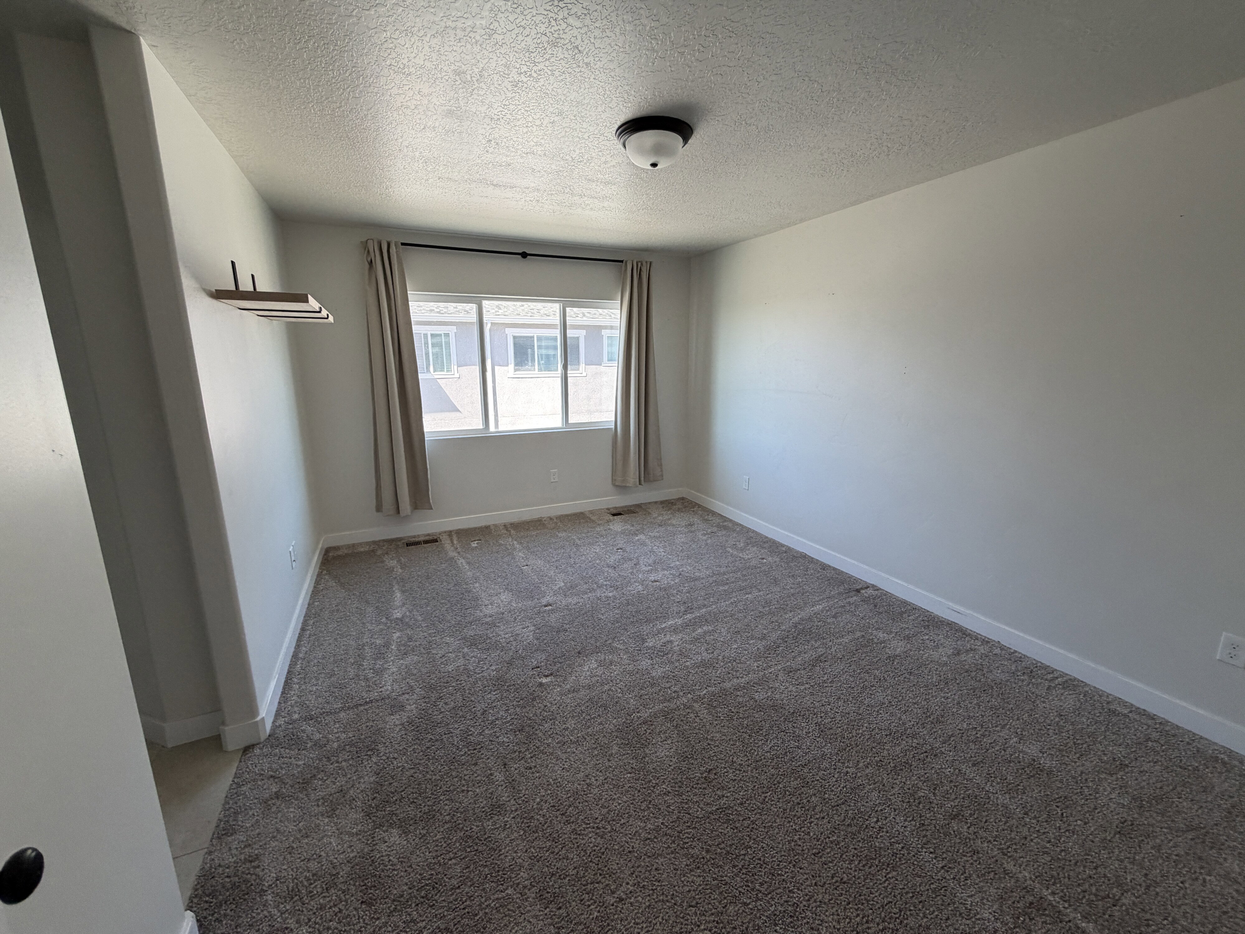 Carpeted room featuring a large window, neutral wall paint, and a built-in floating shelf