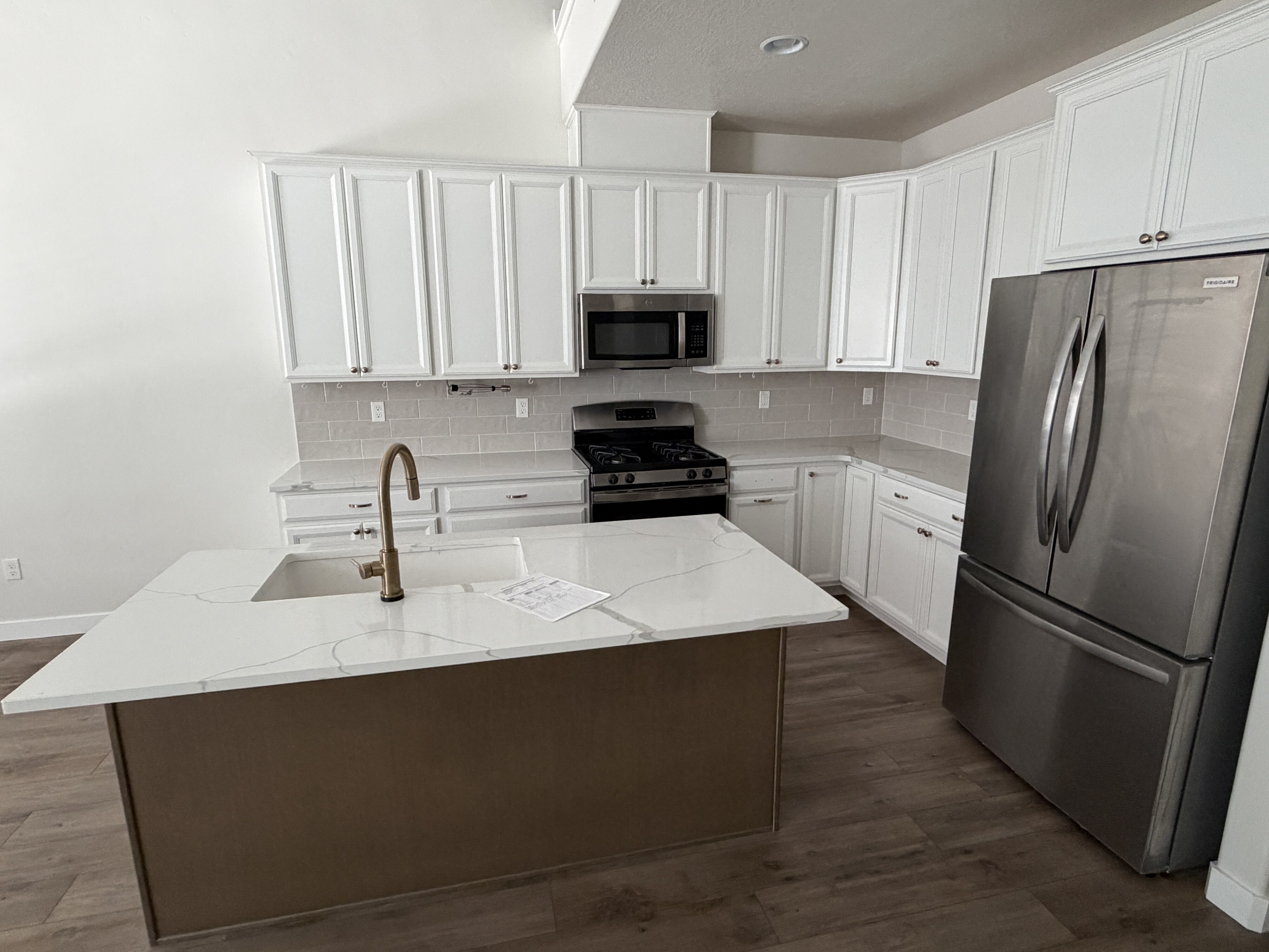 Modern kitchen featuring a central island with an undermount sink, white cabinetry, stainless steel appliances, a subway tile backsplash, and wood-finish flooring