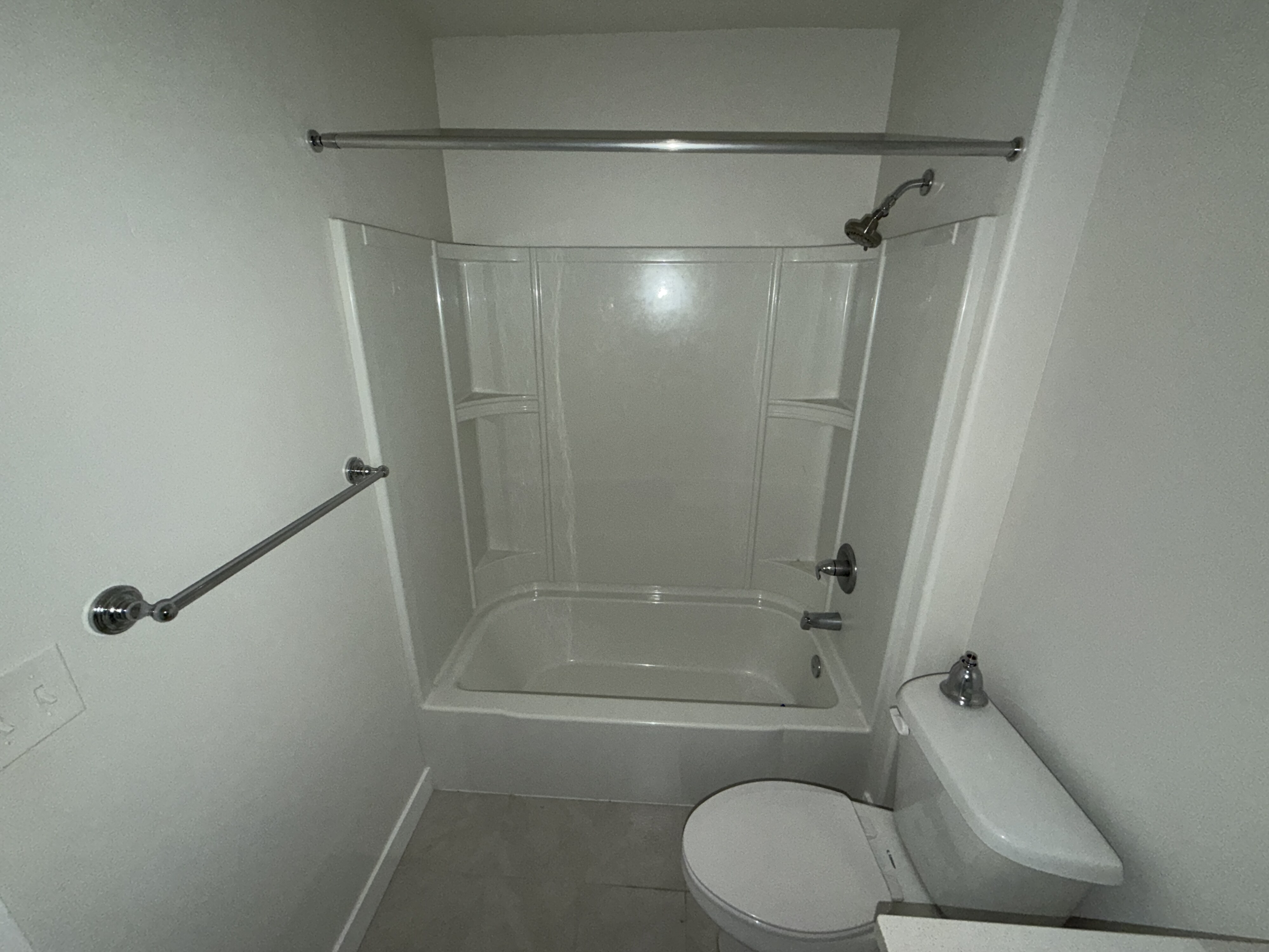 Tub and shower combination with a curved shower curtain rod, chrome fixtures, and a white toilet