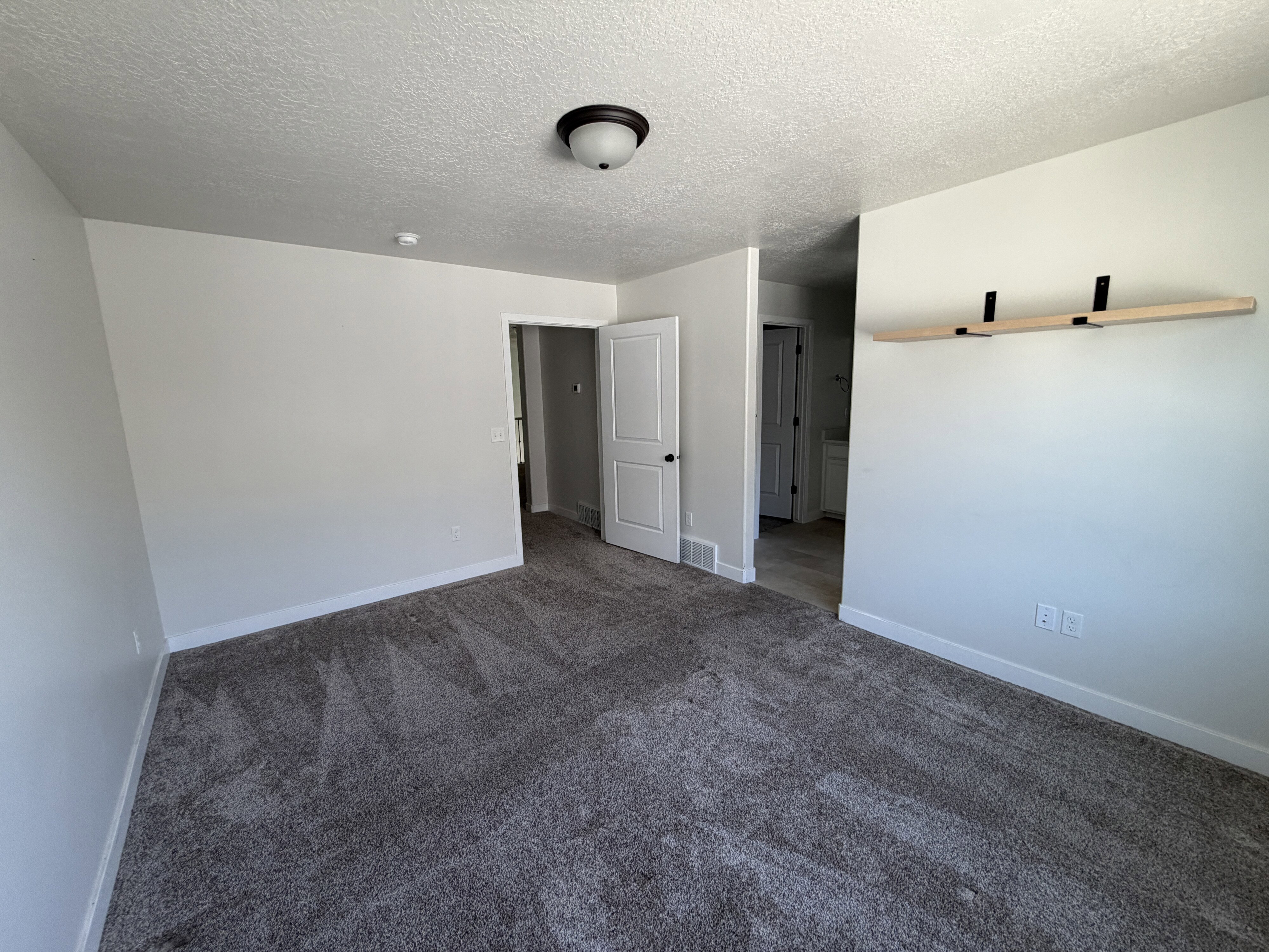 Spacious room featuring neutral paint, textured carpeting, a flush-mount ceiling light, white trim, and a built-in floating shelf