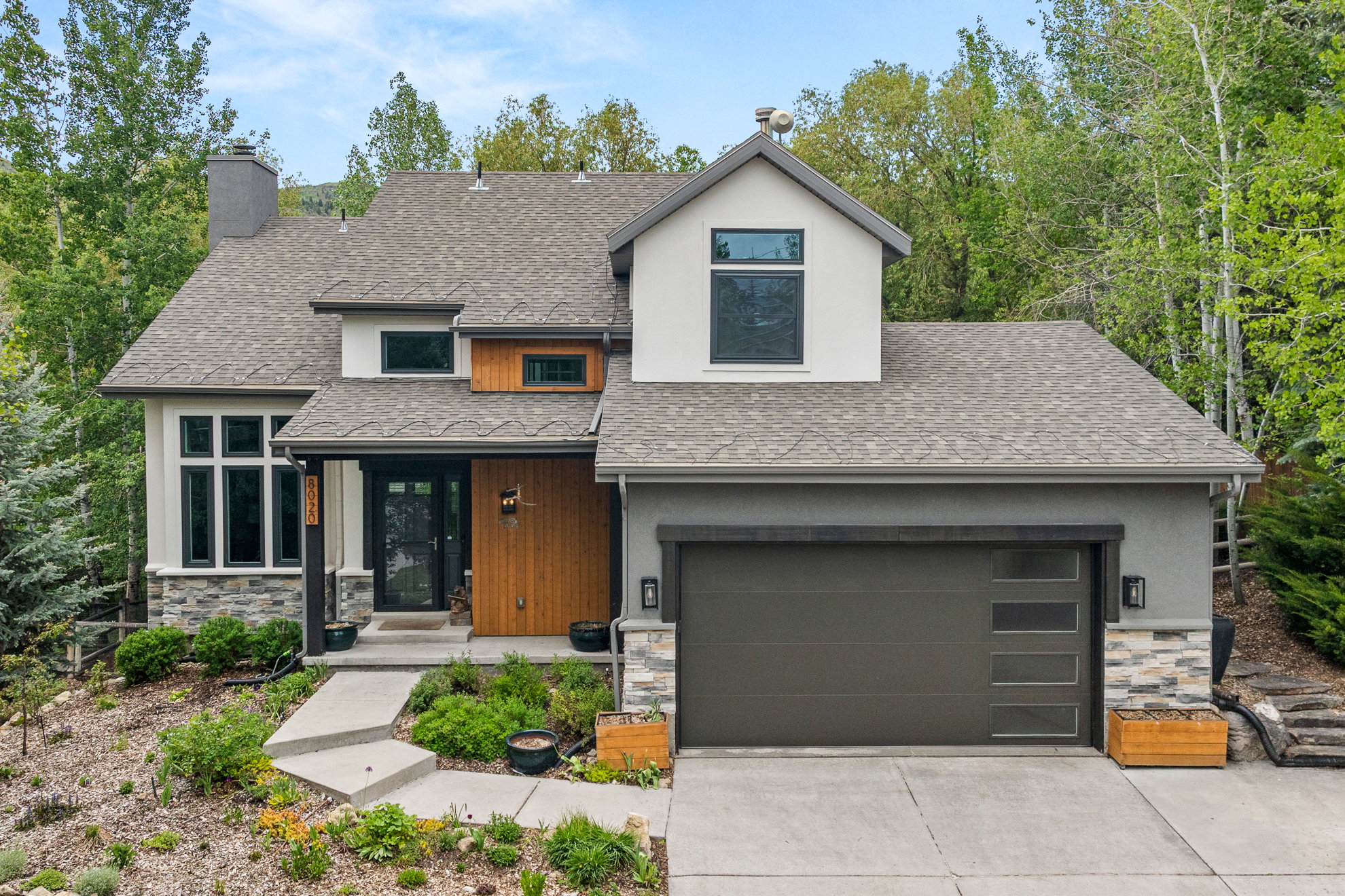 Contemporary architectural design featuring a multi-textured facade with stucco, wood-finish siding, and stone accents