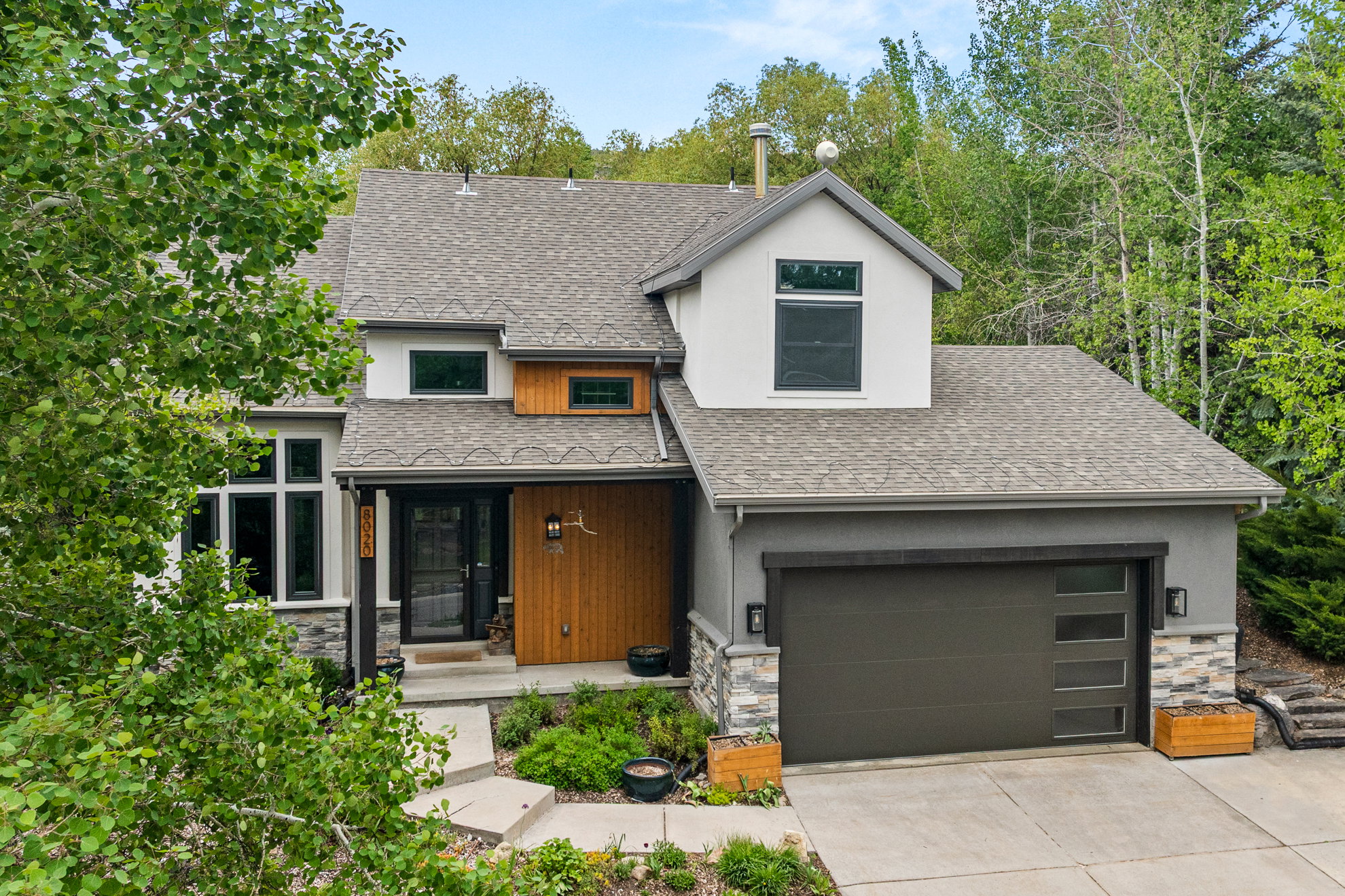 Contemporary-style residence featuring a multi-gabled roofline with asphalt shingles, a stone-clad facade, stucco siding, and wood-paneled accents