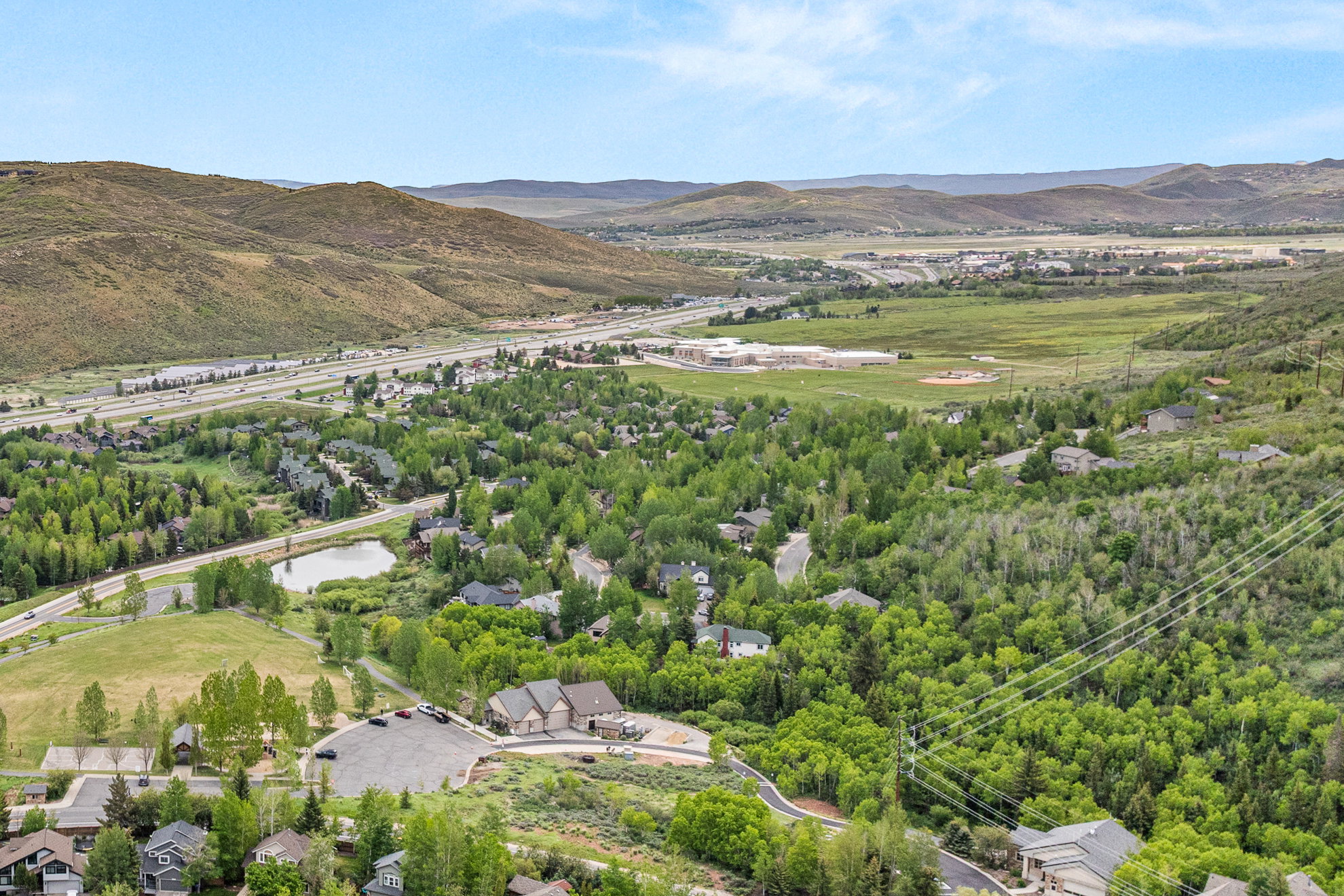Elevated aerial perspective showcasing a residential area amidst extensive green foliage, with a body of water and a highway in the distance
