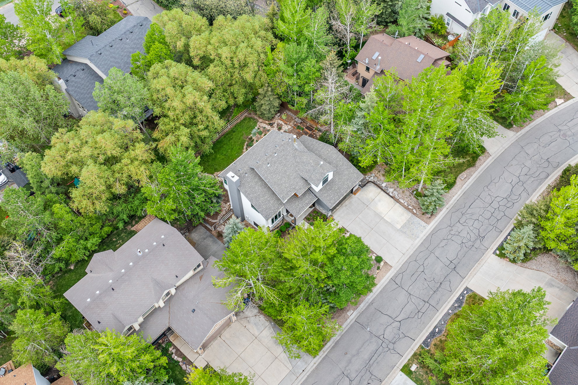 Residential property featuring a multi-level gray shingle roof, attached garage, and mature surrounding trees
