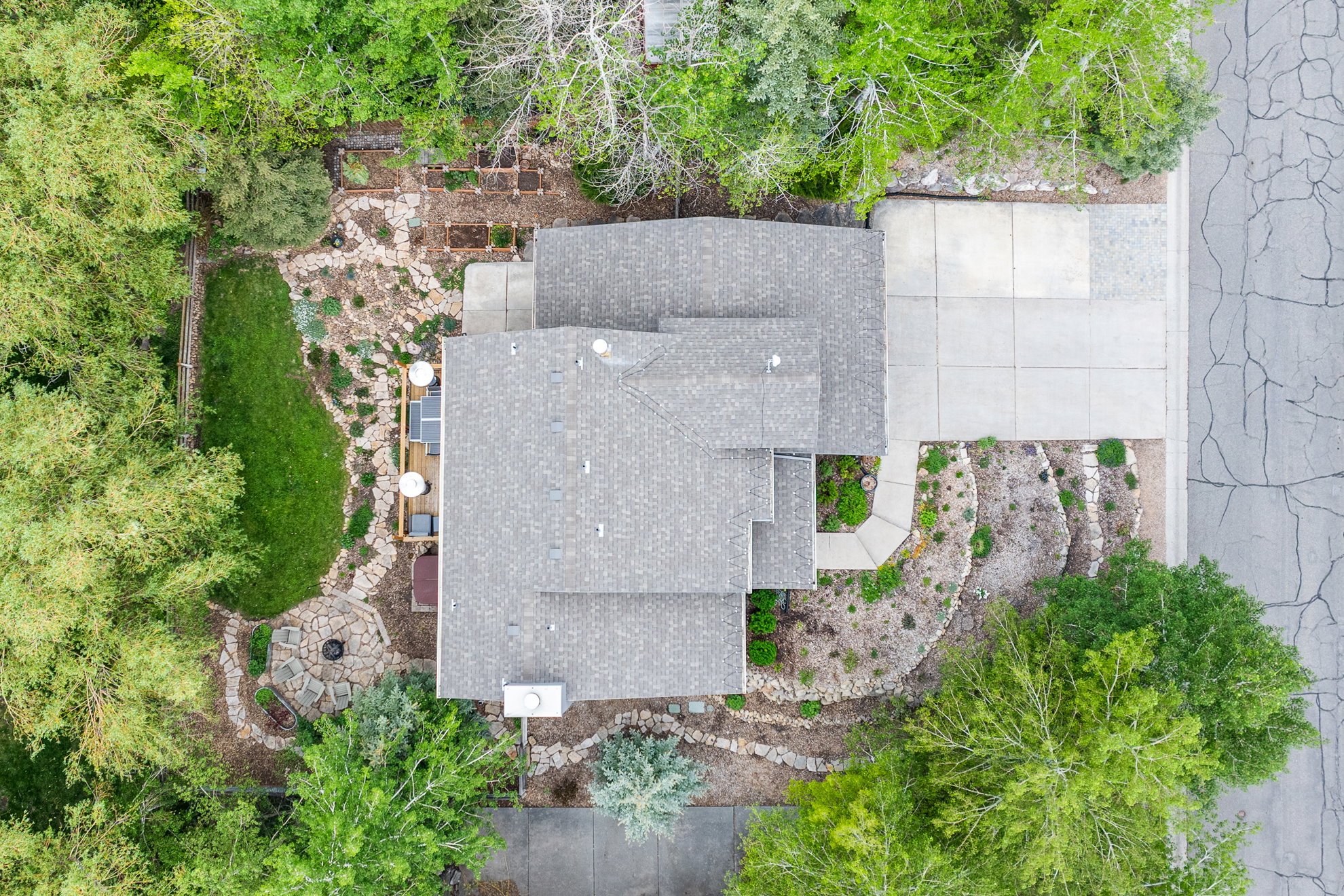 Property featuring a multi-level shingle roof, a concrete driveway, and a stone-paved patio area