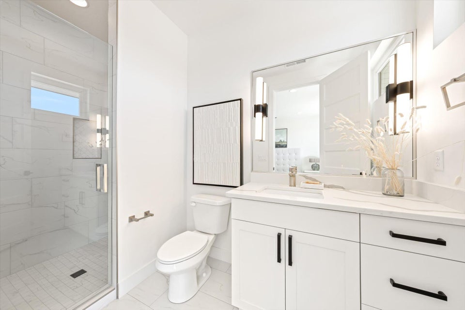 Contemporary bathroom featuring a spacious glass-enclosed shower with a transom window, a white vanity with modern black hardware, a rectangular mirror, and integrated sconce lighting