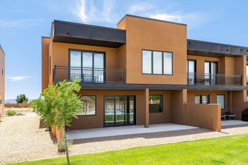 Contemporary stucco exterior featuring multiple balconies, ground-level patios, expansive sliding glass doors, and a manicured lawn