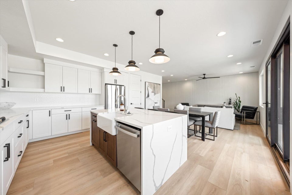 Modern open-concept kitchen featuring a waterfall island with a farmhouse sink, stainless steel appliances, and light wood-finish flooring
