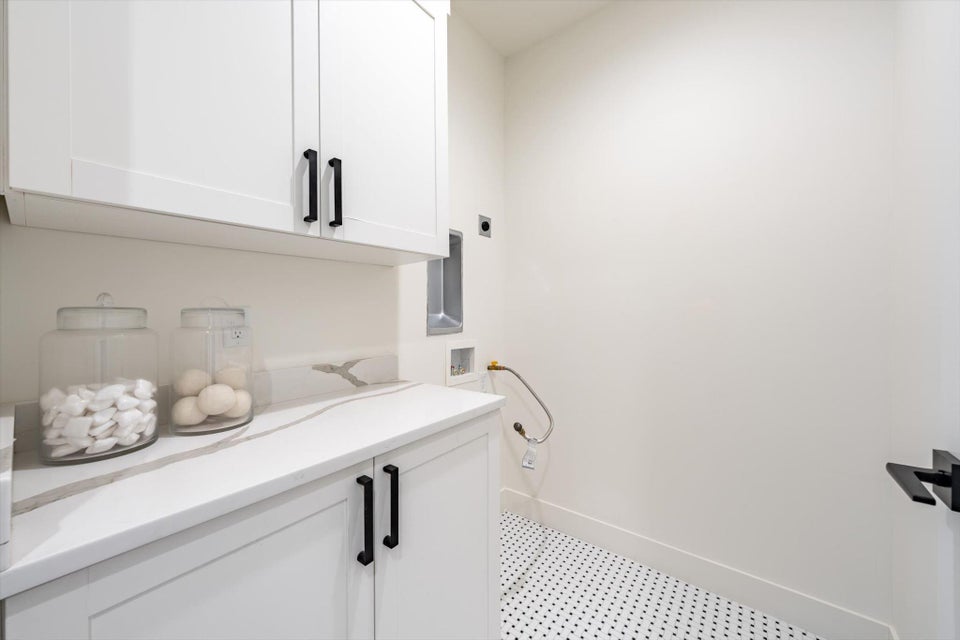 Contemporary laundry area featuring white shaker-style cabinetry with matte black hardware, a light-toned countertop with veining, and hexagonal floor tiling