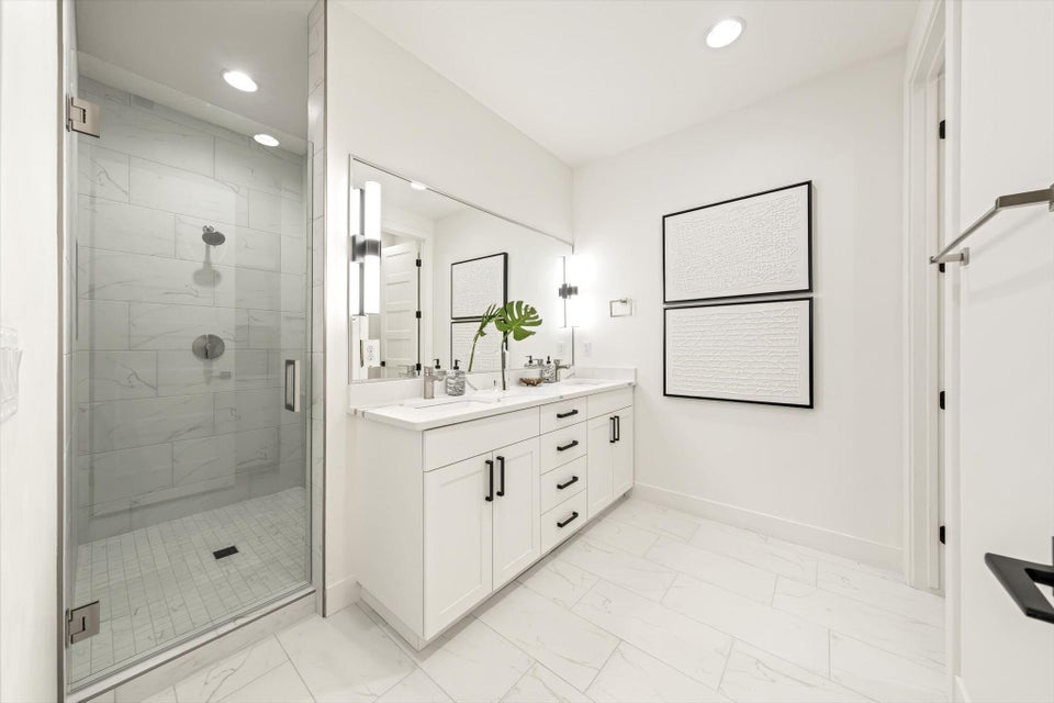 Spacious bathroom featuring a glass-enclosed shower with subway tile, a double vanity with white cabinetry, a large integrated mirror, and wood-finish tile flooring
